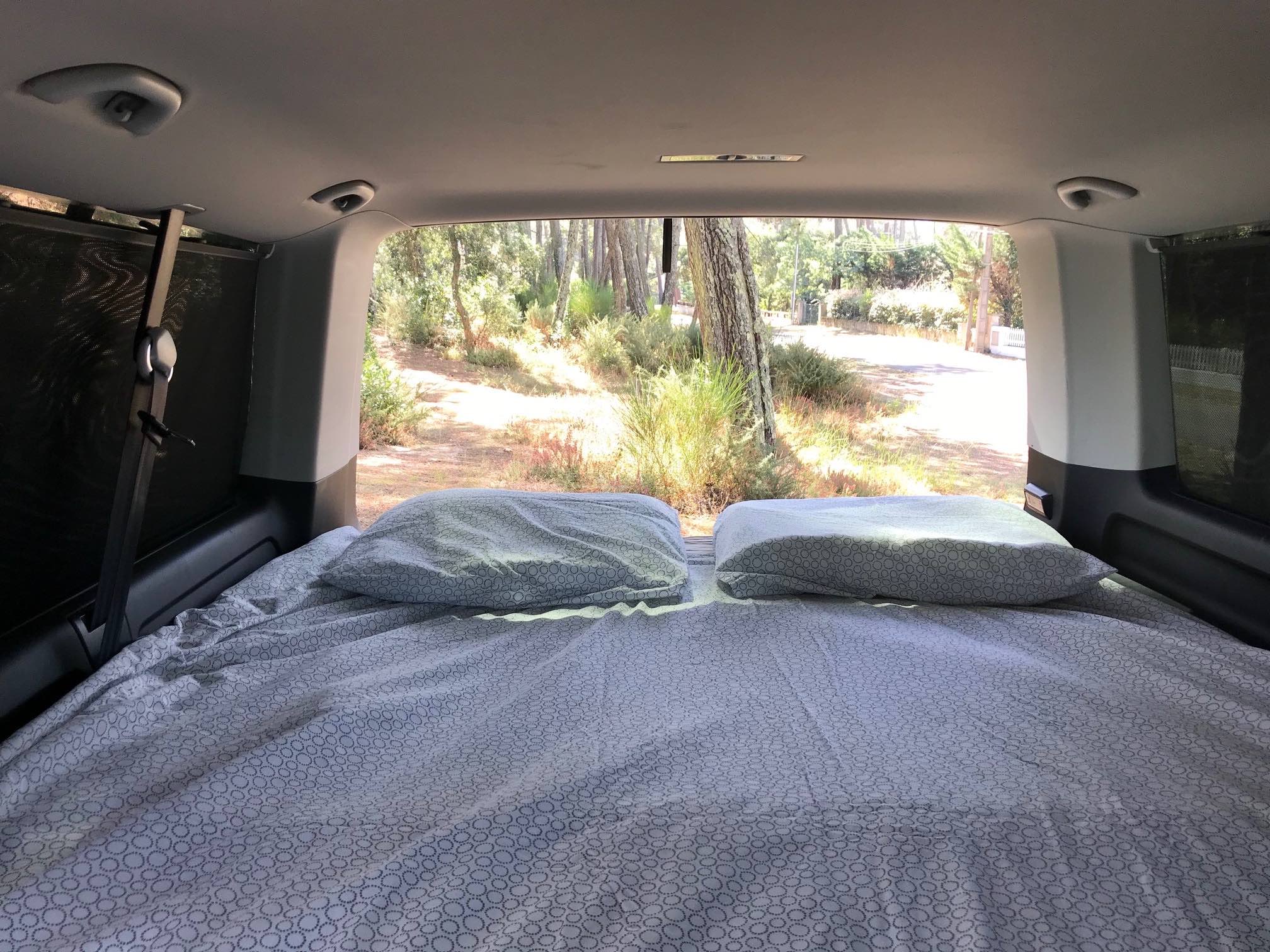 Cozy rv rental interior with a comfortable bed & pillows, looking out at a serene nature view. Perfect for camping.. Volkswagen 4 wheel drive camper 2019