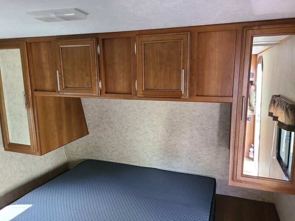 RV rental bedroom interior featuring a blue mattress, overhead wooden cabinets, and mirrored wardrobes for your travels.. Prime Time Avenger 2018