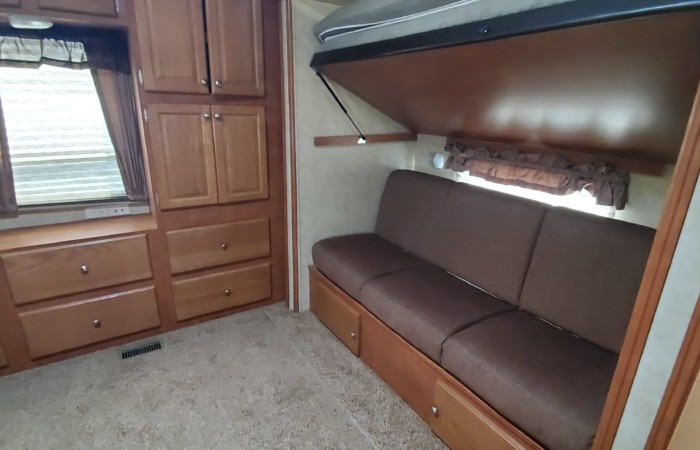 RV rental interior: comfy brown sofa with pull-down bunk bed above, next to wooden cabinets and drawers.. Forest River Cedar Creek Silverback 2012