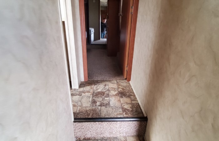 RV rental interior: Narrow hallway with a step down from tile to carpet flooring. Person visible at far end.. Forest River Cedar Creek Silverback 2012
