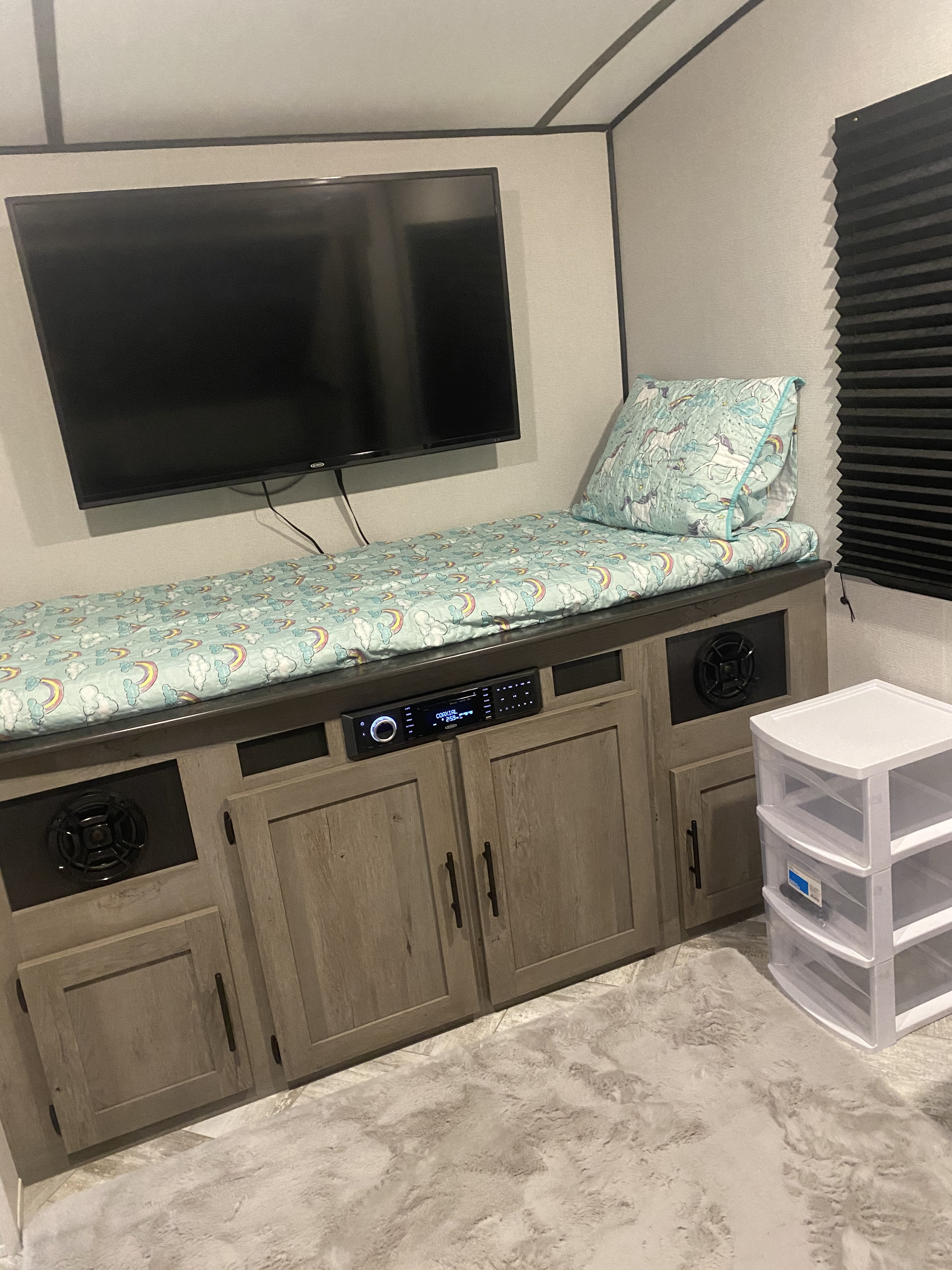 RV rental: A cozy entertainment and sleeping area featuring a TV, stereo, unicorn bedding on a bench, and storage.. Keystone Springdale 2021