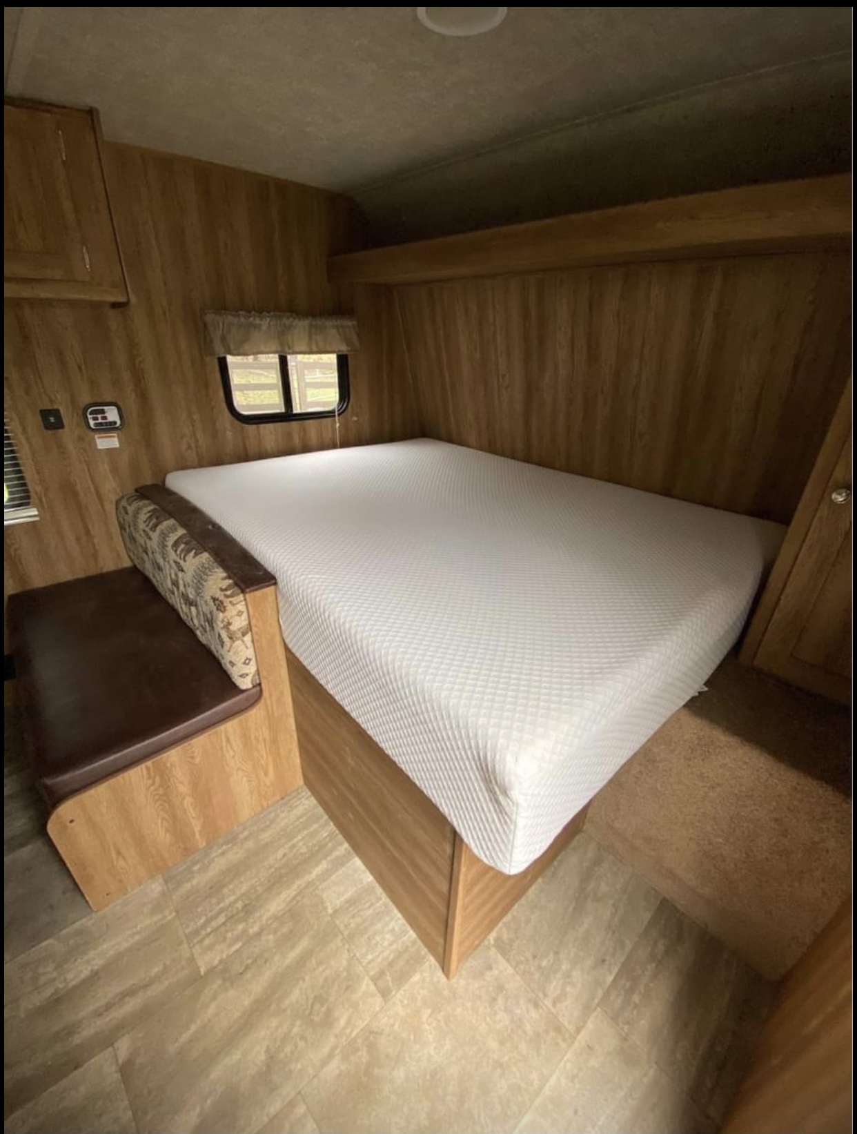 RV rental interior: cozy bed with white mattress, brown bench dinette, wood walls, and mixed flooring.. Keystone Hideout 2016