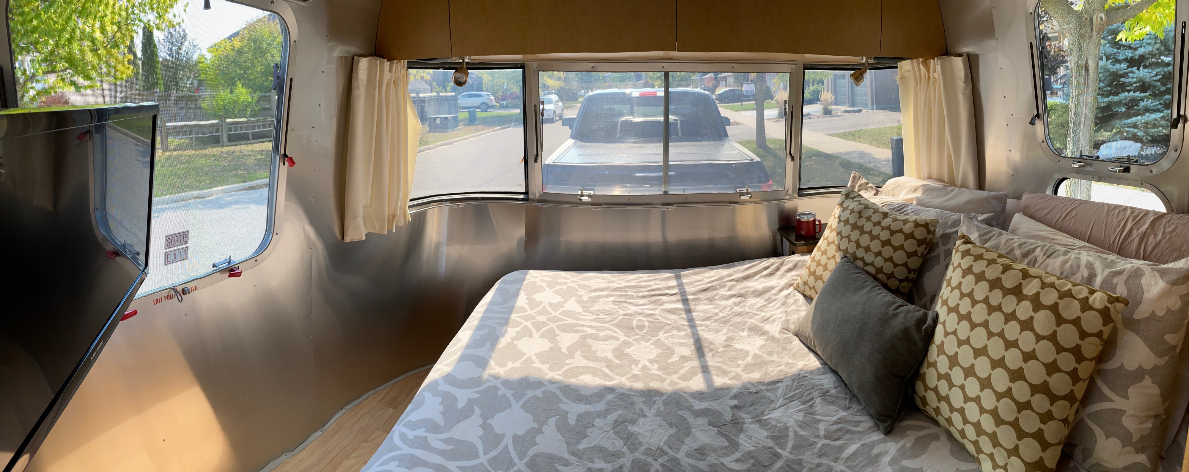 Cozy rv rental bedroom: a bed with patterned linens, pillows, and panoramic windows revealing a street view.. Airstream Flying Cloud 2016