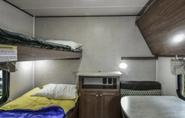 Inside an RV rental: bunk beds, a dining area with patterned seating, and a middle storage cabinet.. Heartland Prowler Lynx 2018
