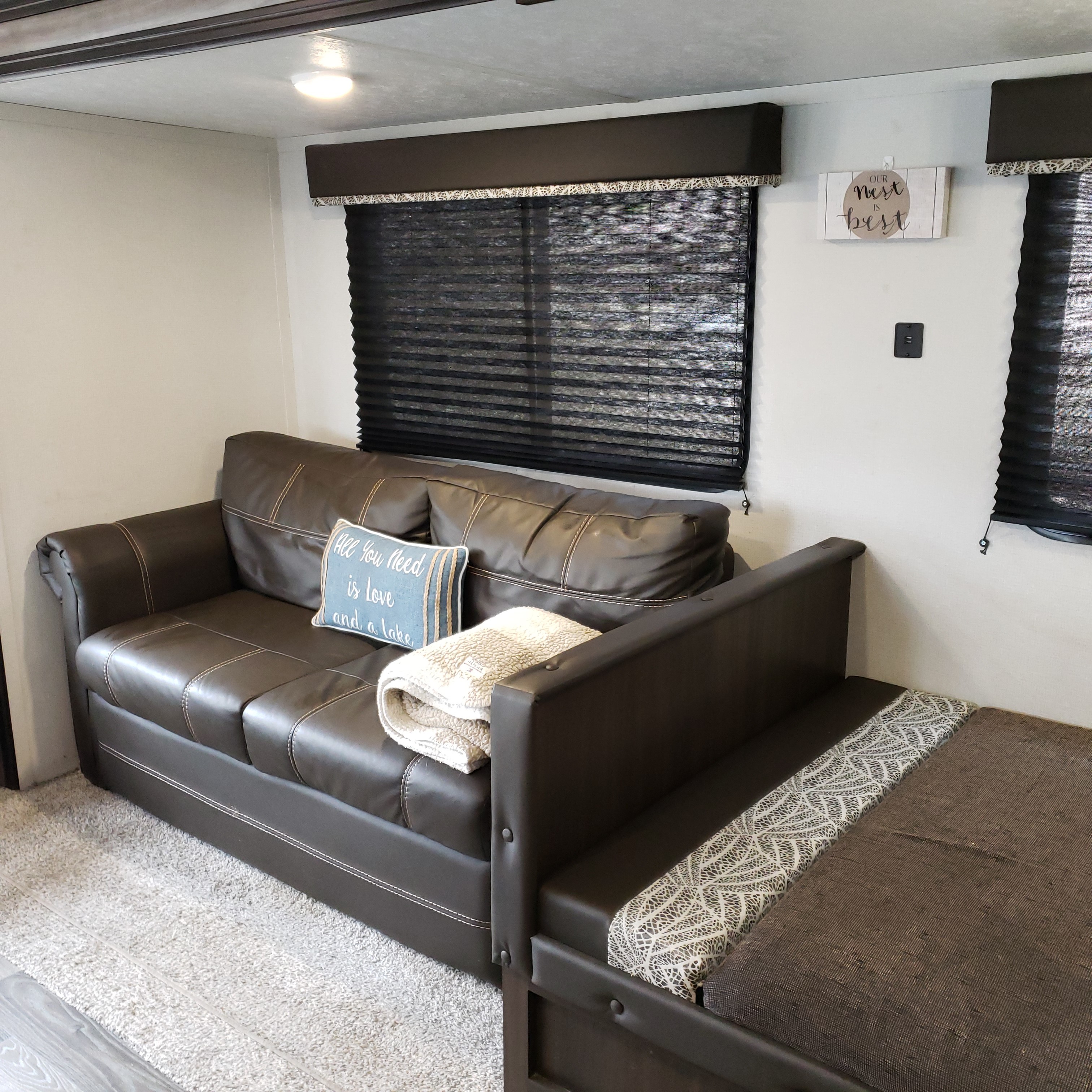 Brown leather sleeper sofa and lounge area in an RV rental, with dark window blinds and a light carpet.. Keystone Springdale 2020