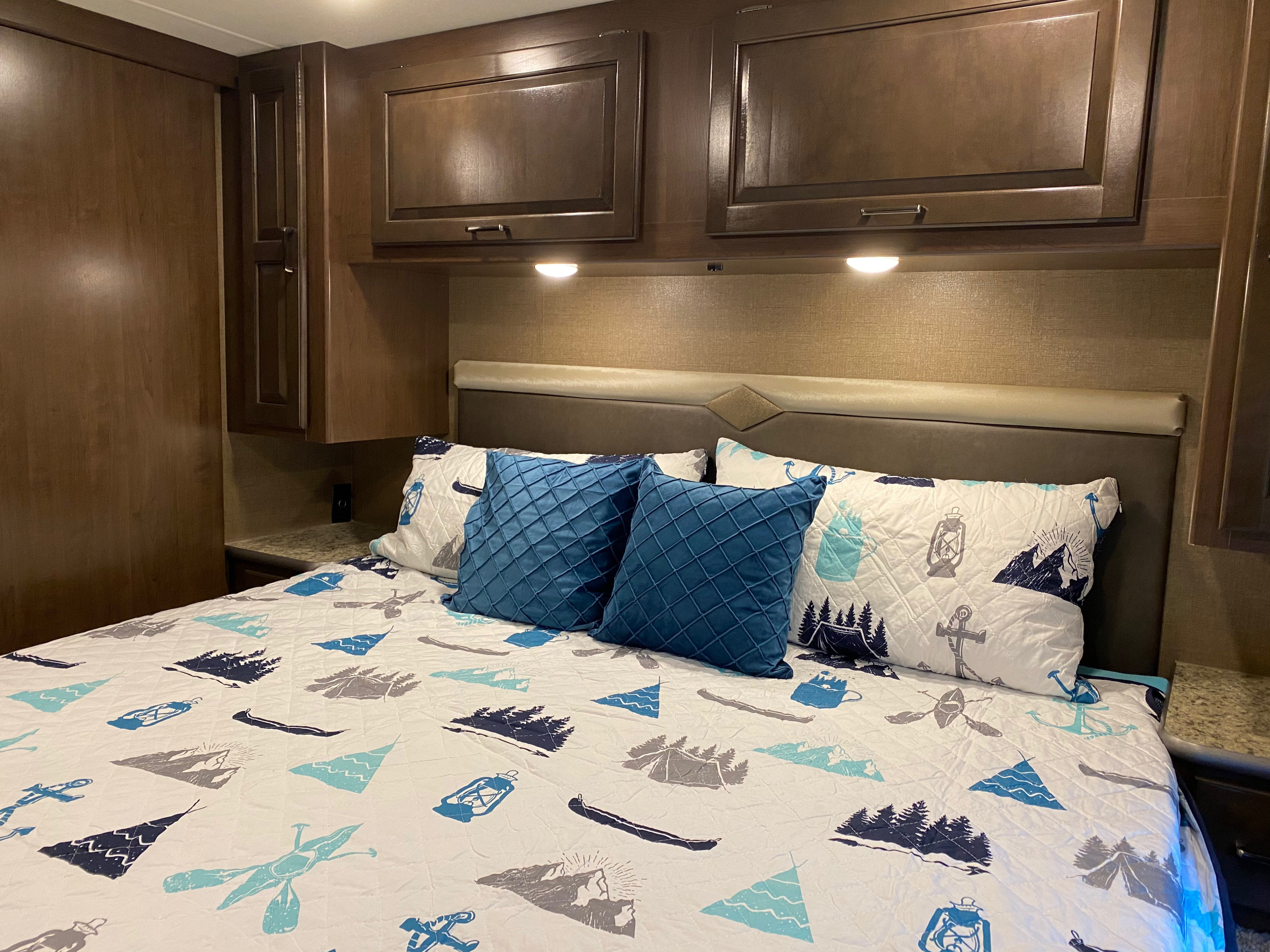 Cozy RV rental bedroom featuring outdoor-themed bedding, overhead cabinets, and a comfortable headboard. Ready for adventure.. Thor Hurricane 2019