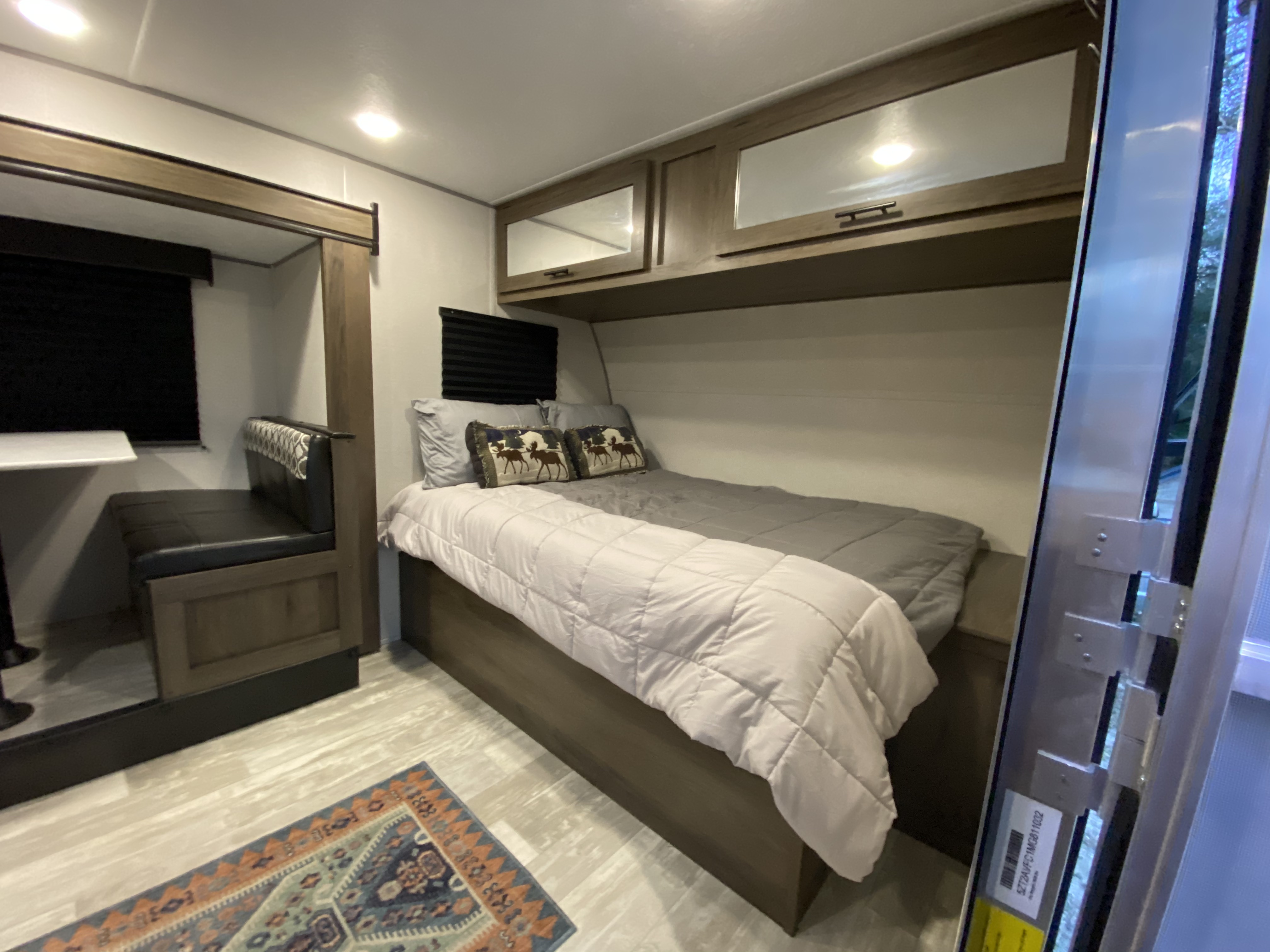 Explore this RV rental's cozy interior, featuring a main bed with overhead storage and a compact dinette on the left.. Prime Time Avenger 2021