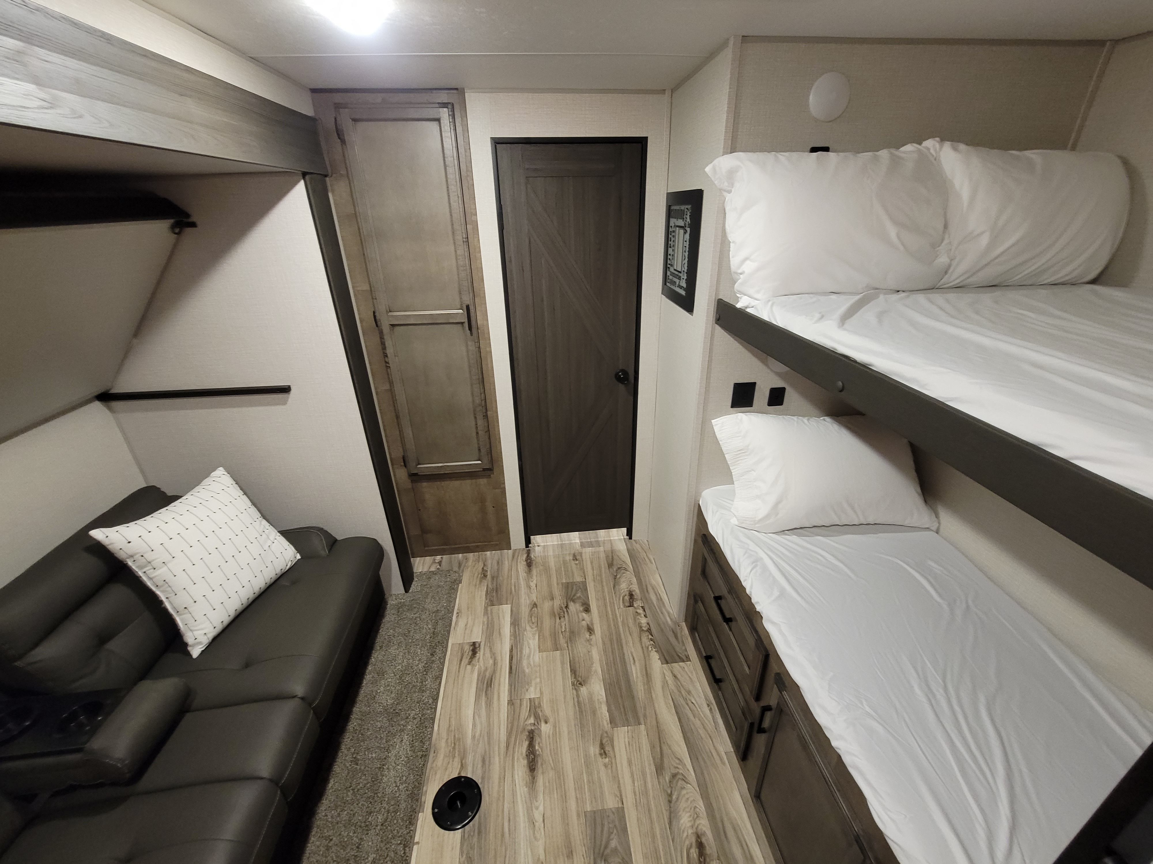 Modern RV rental interior: dark sofa, wooden doors, wood-look floor, and comfortable bunk beds with white linens.. Venture ST332VBH 2021