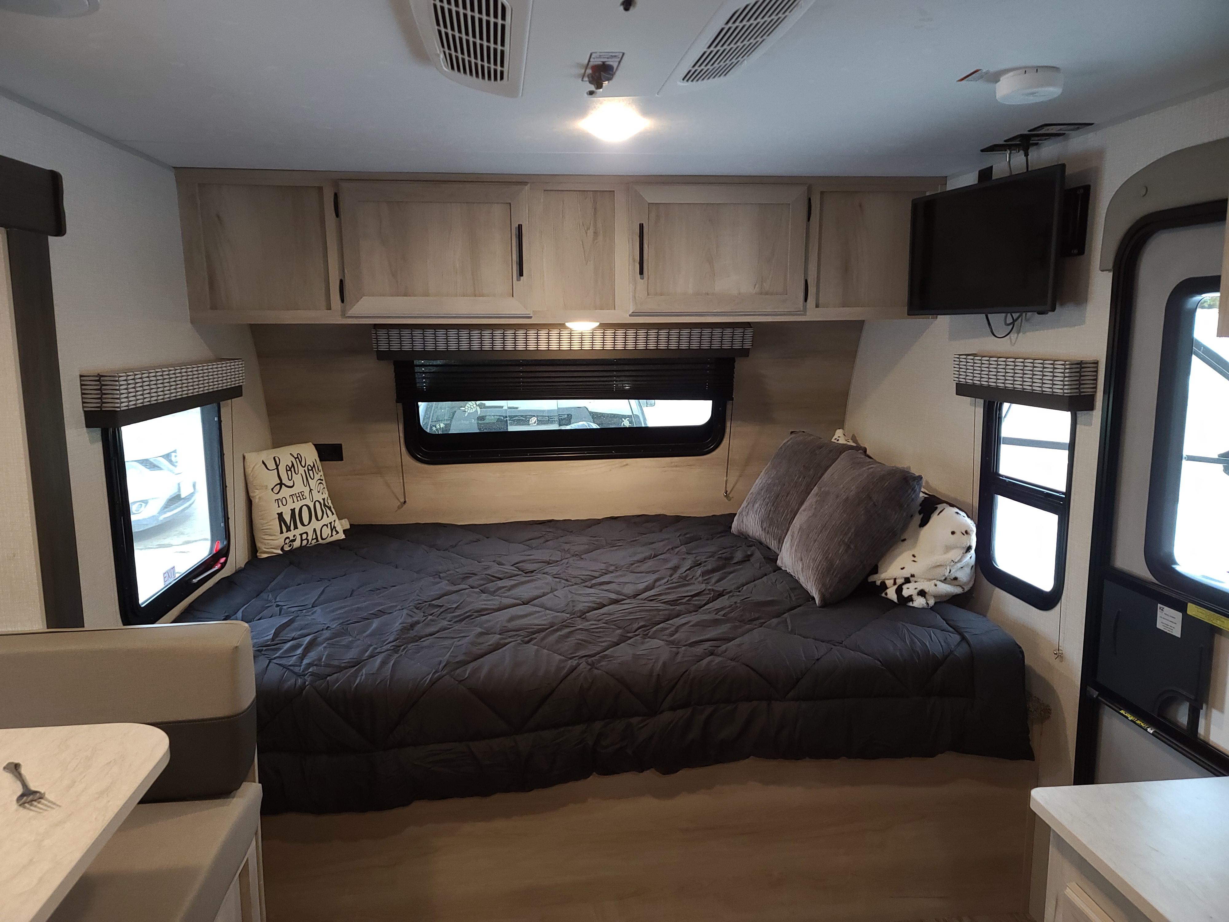 Cozy RV rental interior: large bed, overhead storage, a TV, and a dinette area visible on the left.. K-Z Manufacturing Escape 2021
