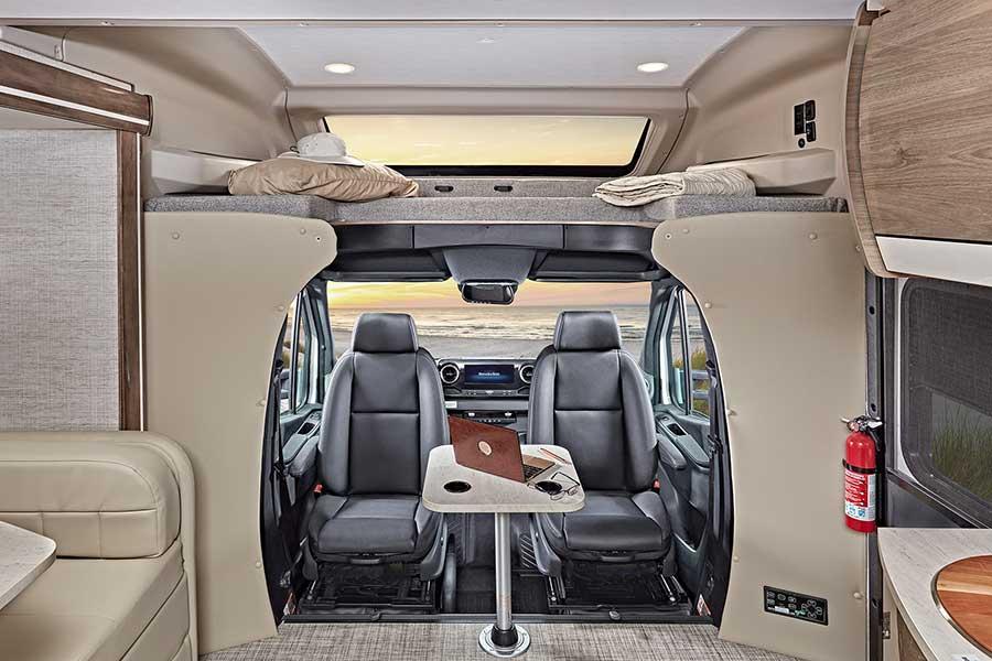 This RV rental interior features a cozy loft bed, versatile front seating with a table for work, and stunning ocean views.. Entegra Coach Qwest 2021