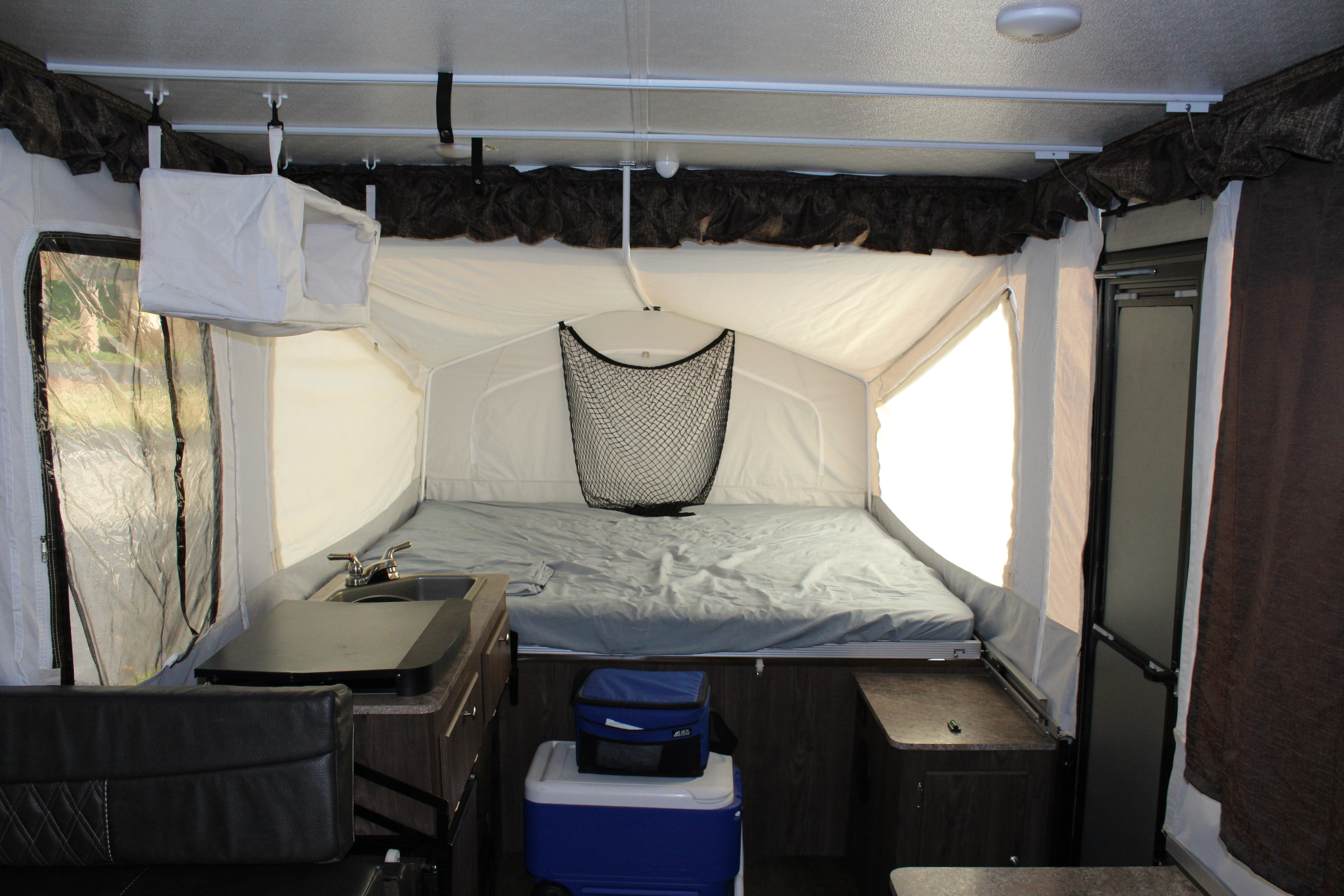 RV rental pop-up camper interior, showing a bed, kitchen with sink, and seating area. Soft walls create a comfortable camping space.. Forest River Rockwood ESP 2017