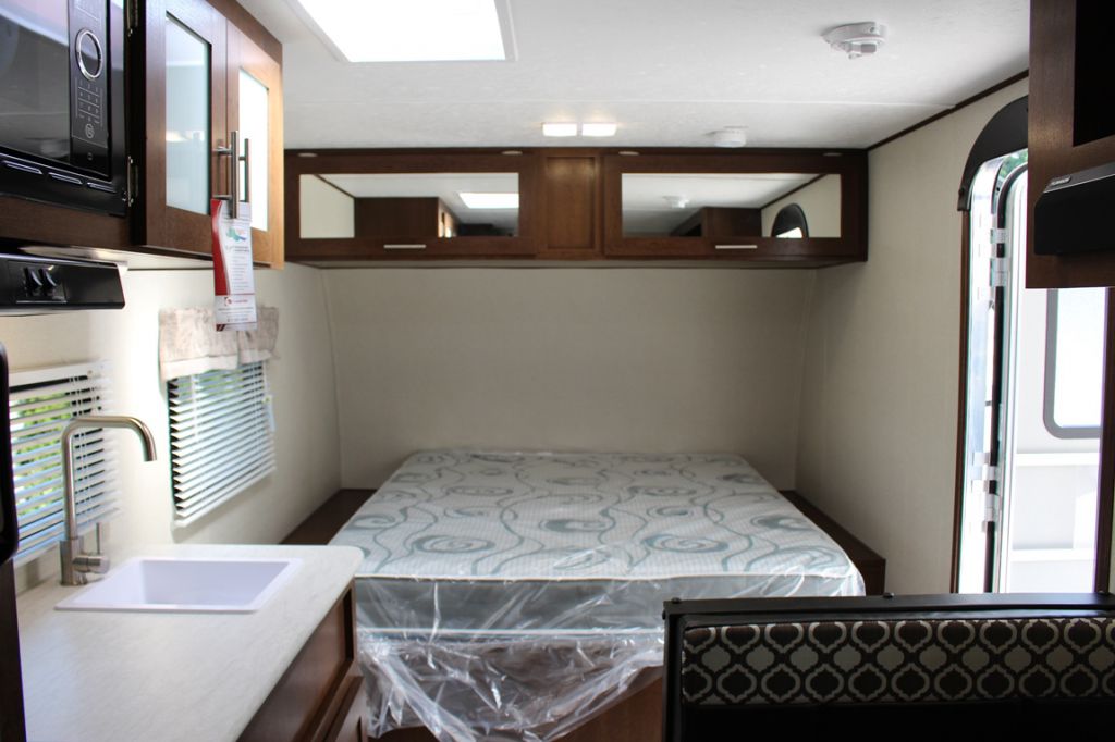 Inside a clean RV rental: a comfortable bed, a compact kitchen with sink and microwave, plus overhead storage.. Prime Time NAVI 2019