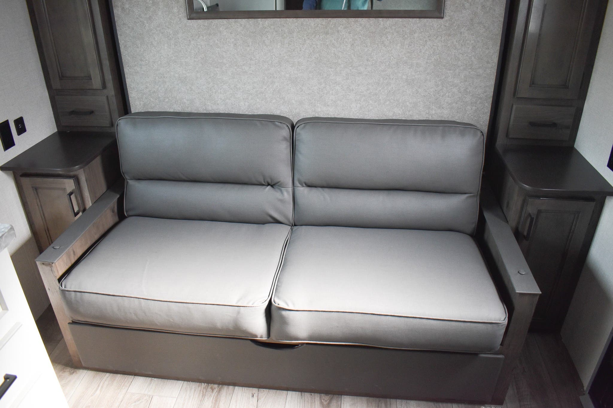 Cozy grey pull-out RV sofa bed, flanked by wood cabinets, in a modern RV rental. Compact living comfort.. Open Range 20MB 2021