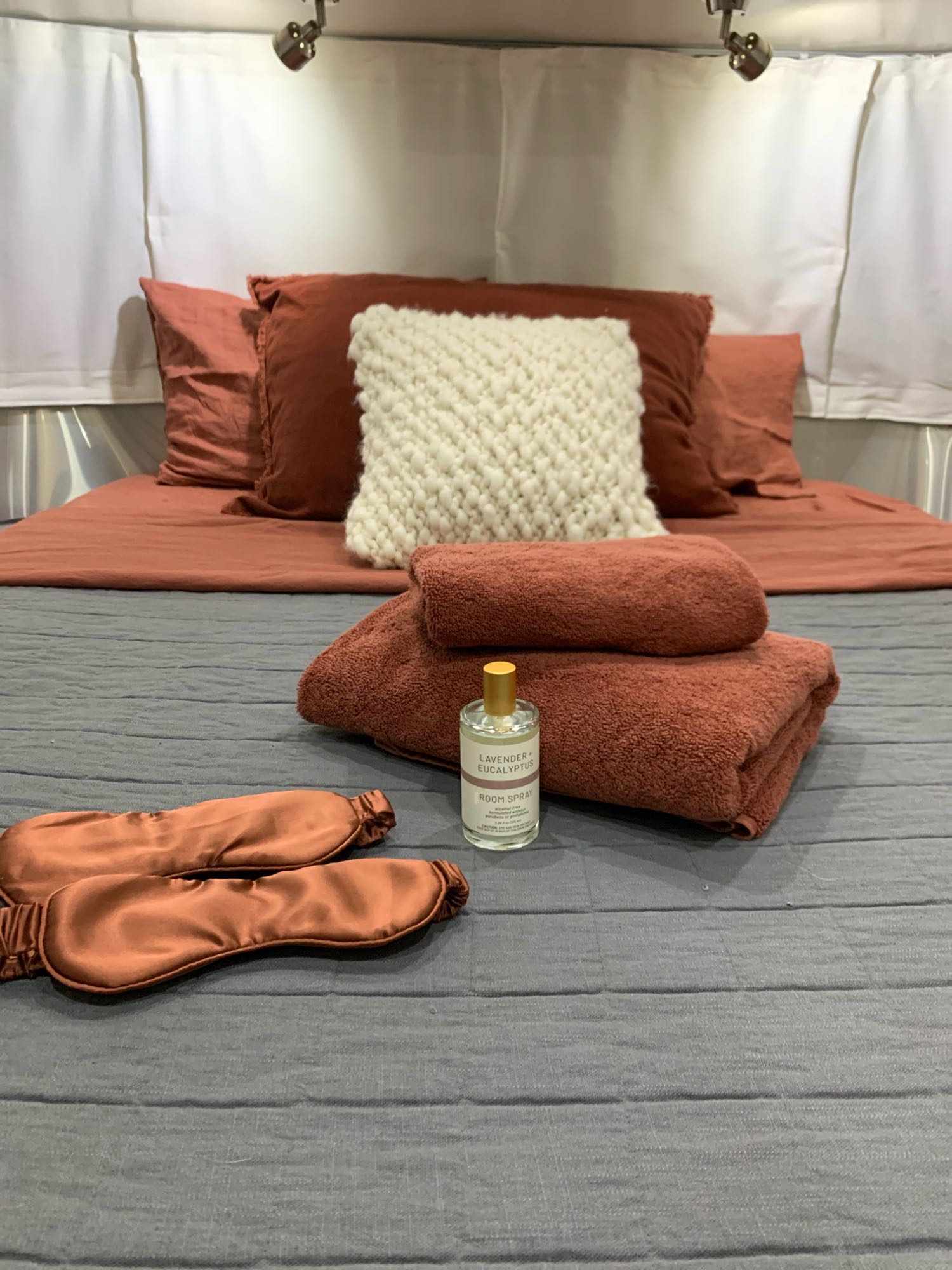 Cozy RV rental bedroom with terracotta bedding, towels, sleep masks, and room spray for comfort.. Airstream Serenity 2018