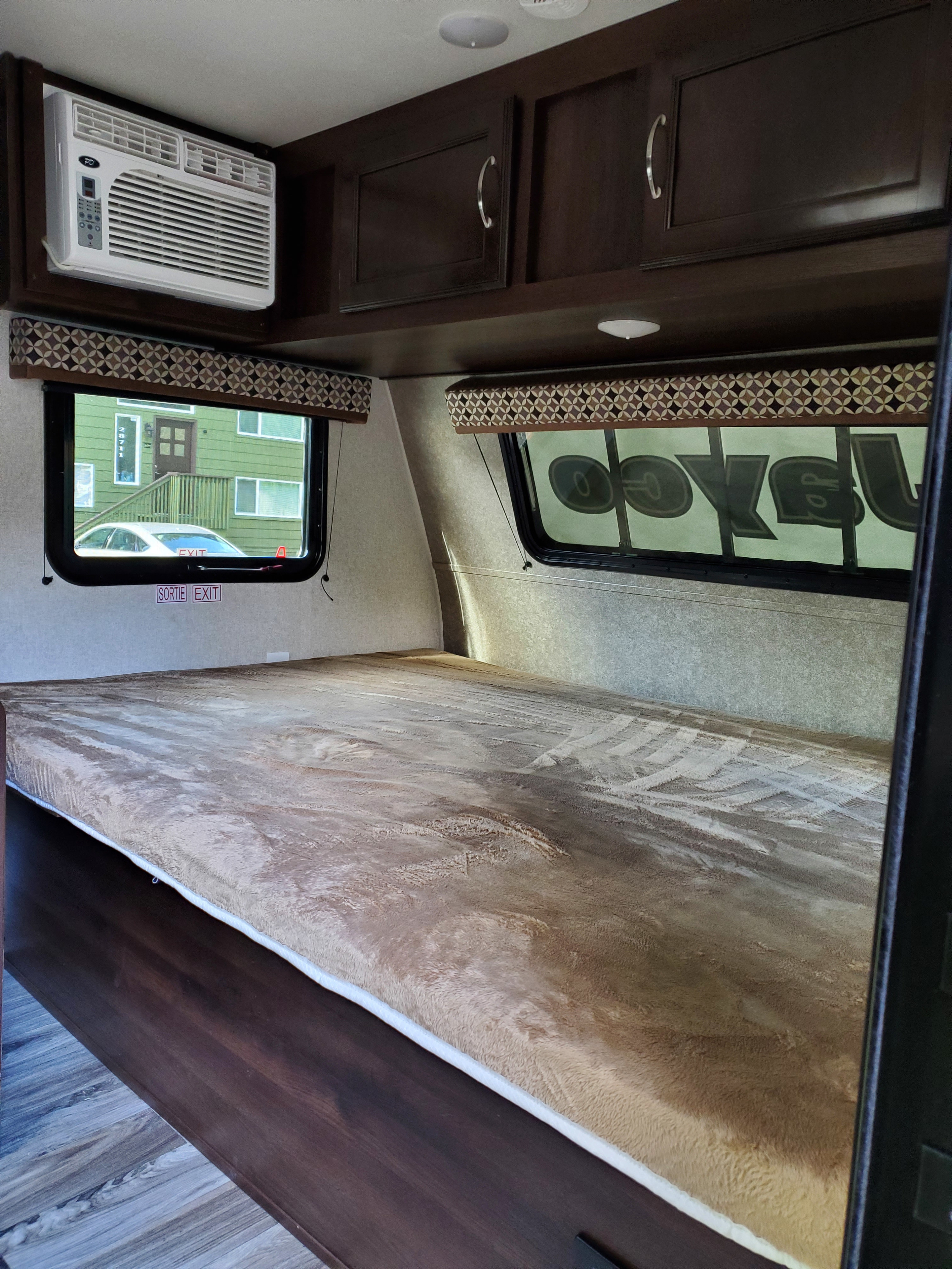 RV rental bedroom interior featuring a large bed, wall-mounted AC, and overhead cabinets for storage.. Jayco Baja 2018