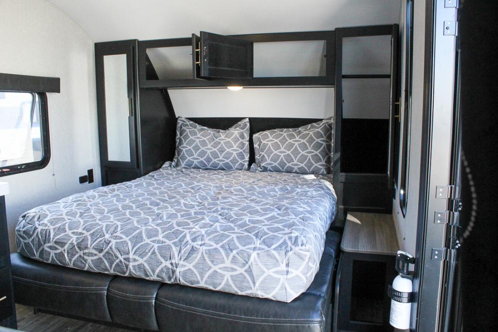 Cozy RV rental bedroom with gray patterned bedding, black cabinetry, and a window. Includes a fire extinguisher.. Forest River Cherokee Grey Wolf 2021