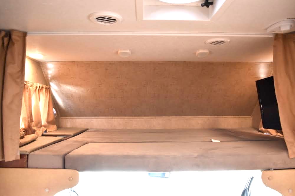 Spacious and comfortable cab-over bed in an RV rental, featuring a mattress, curtains, and TV for a cozy stay.. Forest River Sunseeker 2015
