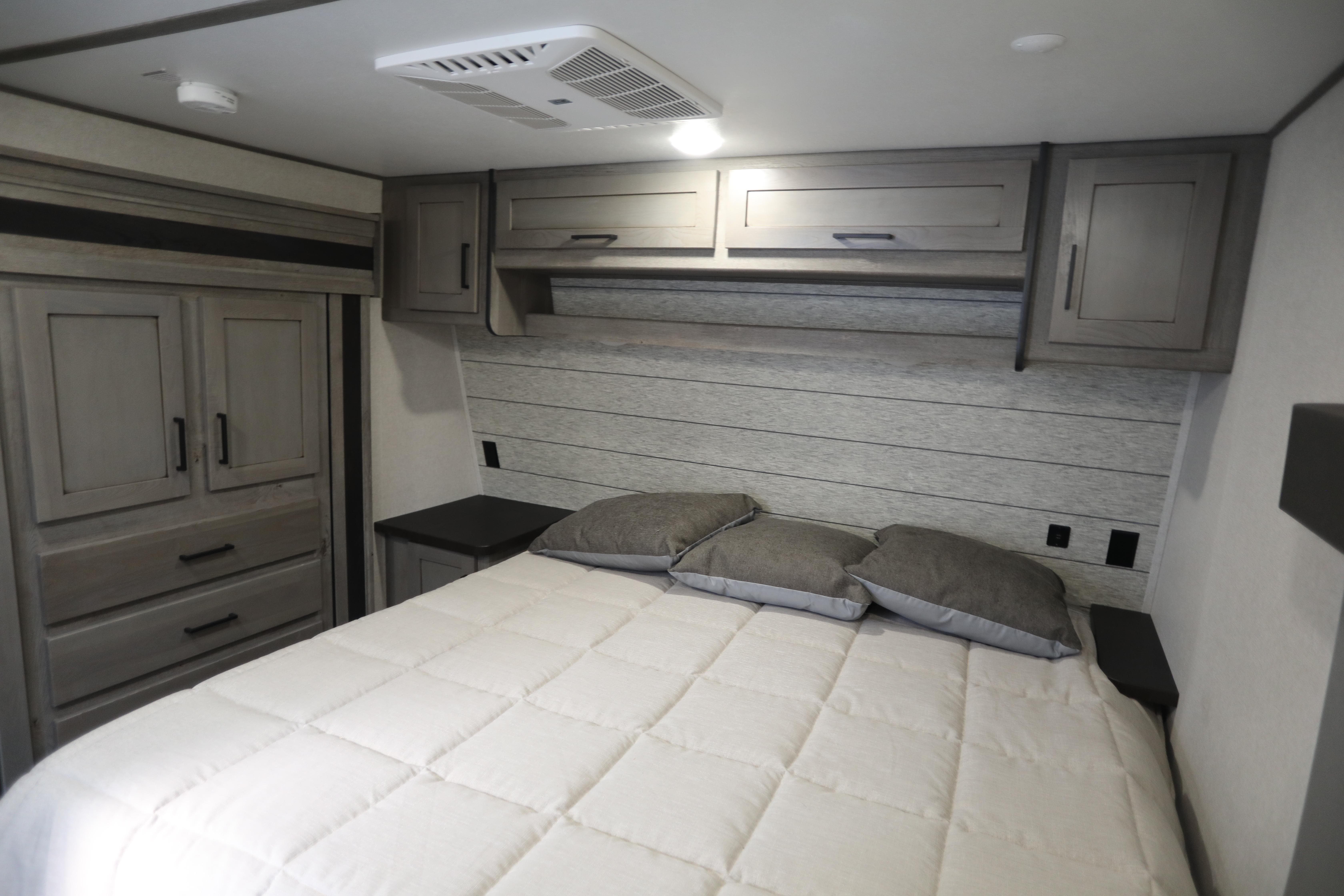 Cozy RV rental bedroom with a comfy bed, modern wood-look cabinets, and wardrobe storage for your travels.. Keystone Raptor 2020