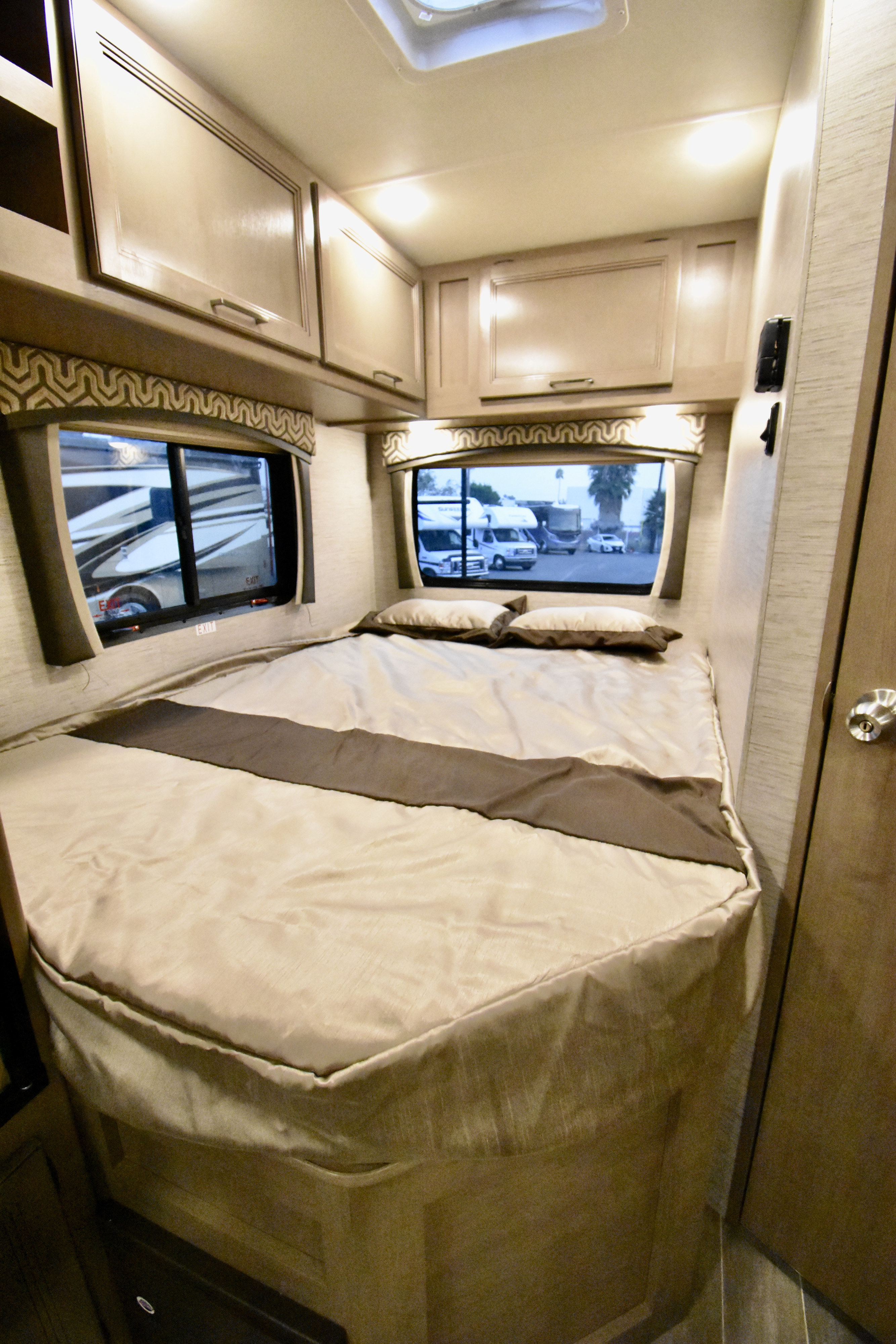 Explore a comfortable RV rental bedroom featuring a cozy bed, overhead storage, and scenic window views.. Thor Chateau 2021