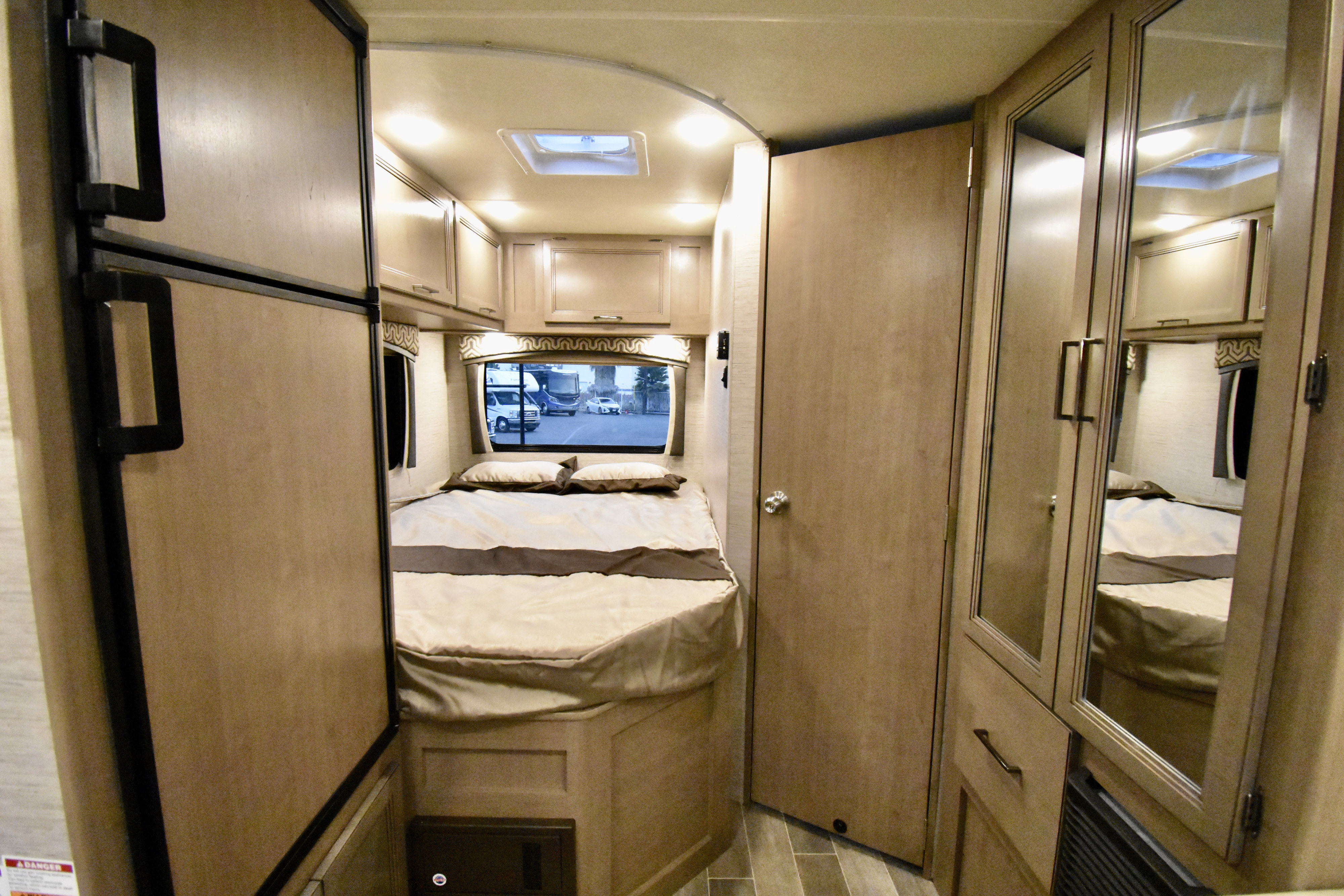 This RV rental bedroom offers a cozy bed, overhead storage, refrigerator, and mirrored closet. Ideal for travel.. Thor Chateau 2021