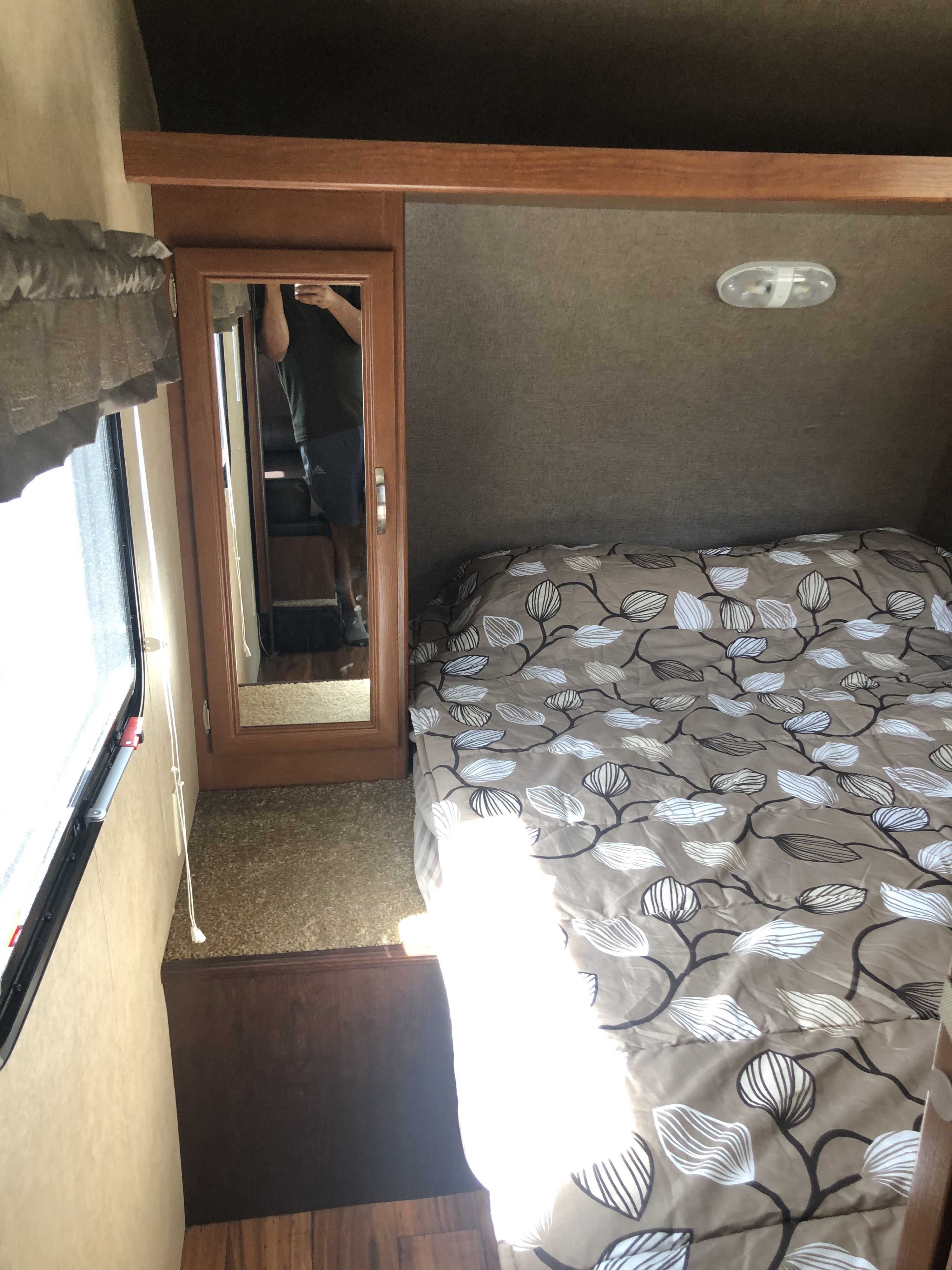Inside an RV rental: a compact bedroom featuring a comfortable bed with a leaf-patterned comforter, window, and mirror.. Forest River Wildwood X-Lite 2015