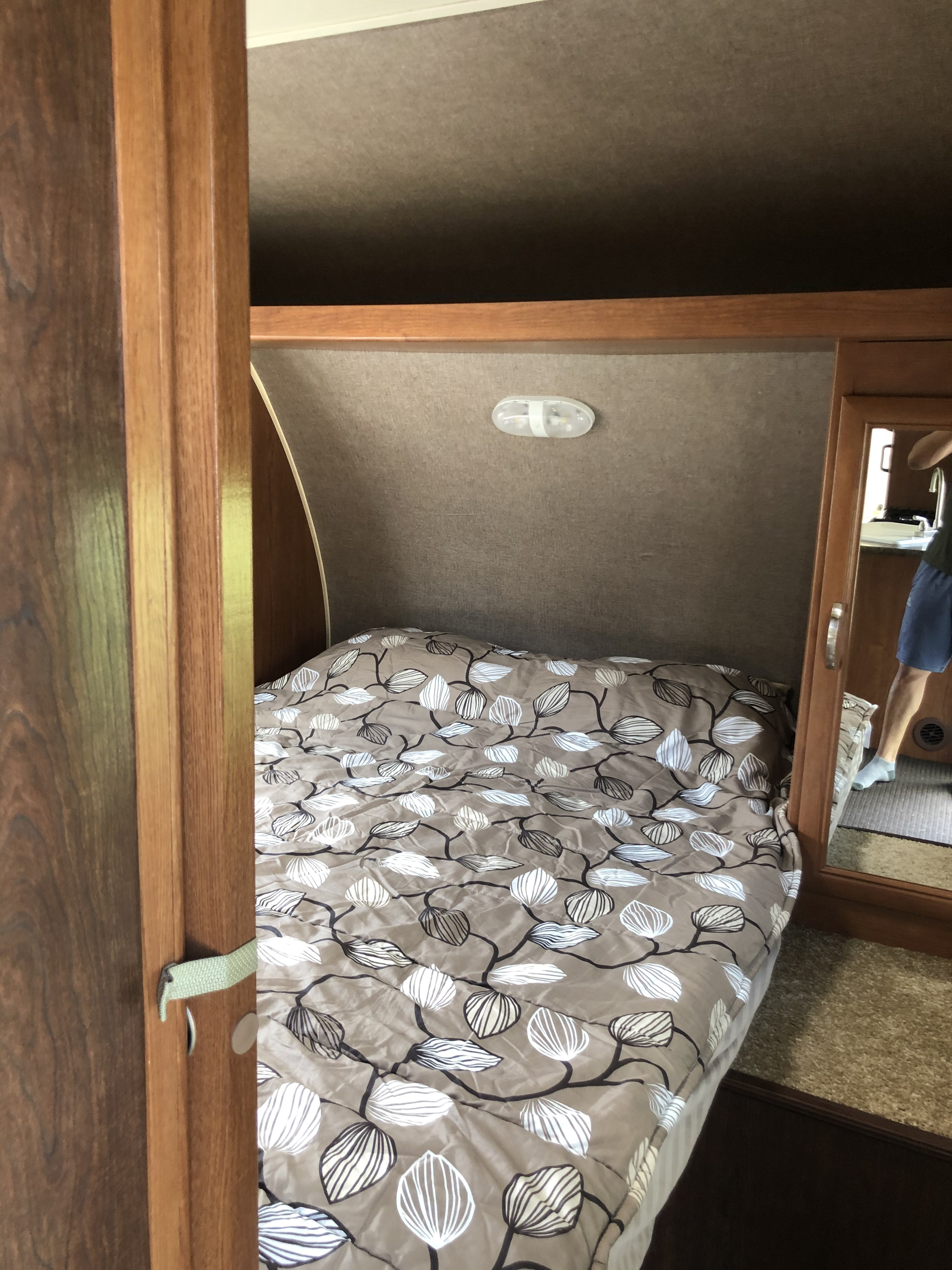 RV rental interior: A compact bedroom features a bed with a leaf-patterned comforter, an overhead light, and mirrored storage.. Forest River Wildwood X-Lite 2015