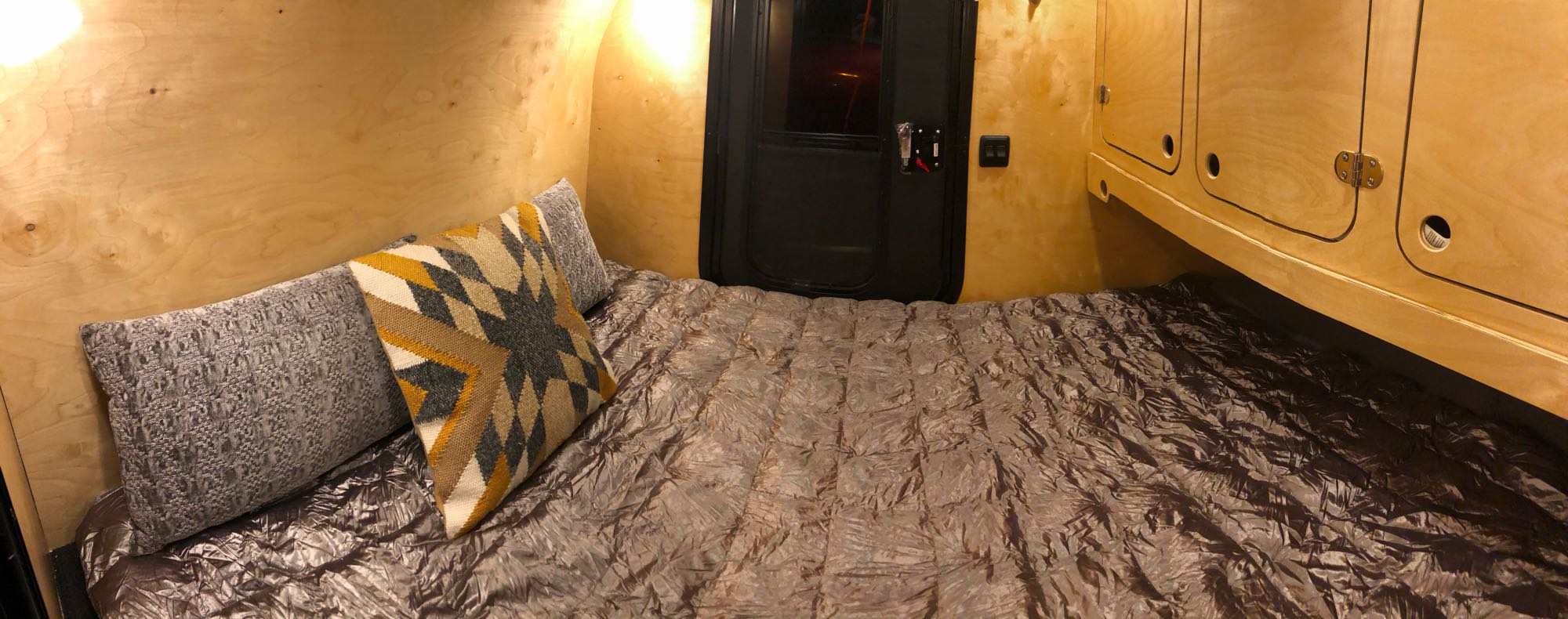 Cozy RV rental interior shows a bed with pillows, wood walls, a dark door, and built-in storage cabinets.. Other Other 2021