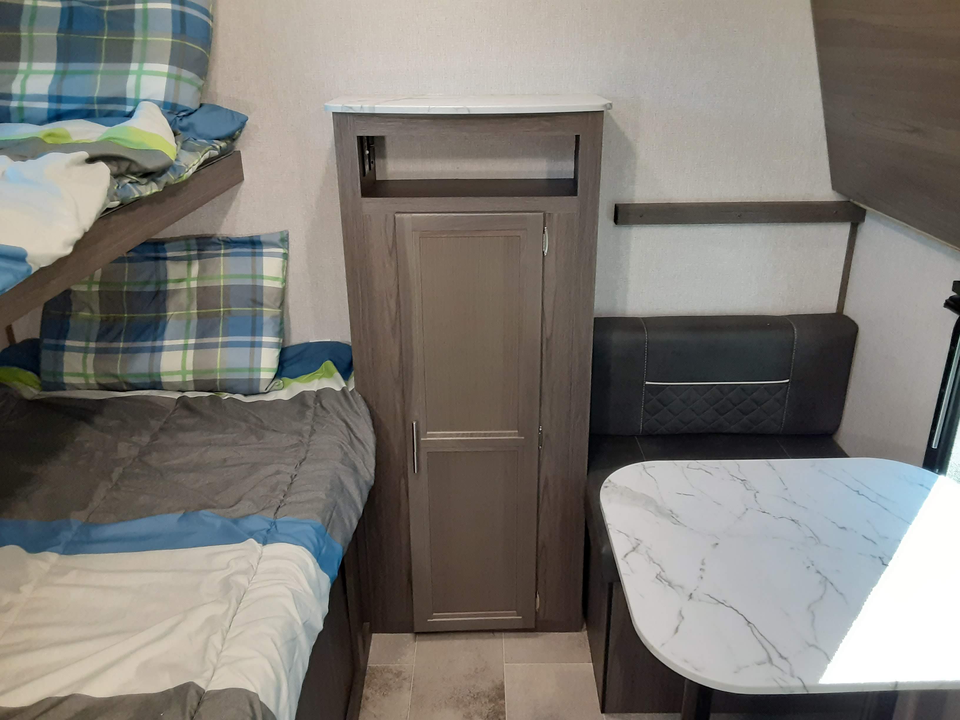 Inside an RV rental, featuring bunk beds, a central cabinet, and a dinette with a white marble table.. Dutchmen Kodiak 2020