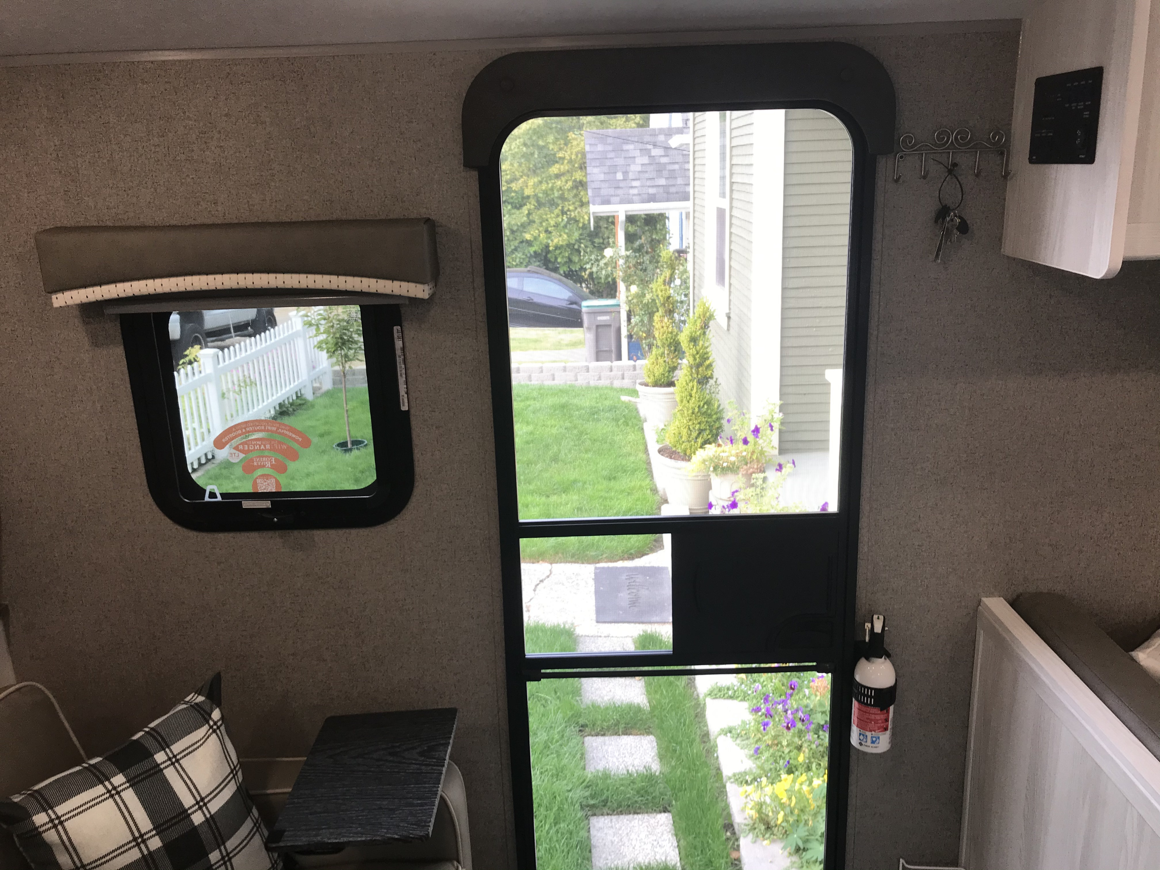 RV rental interior view: window with outdoor scene, screen door, key hooks, monitor panel, and fire extinguisher.. Forest River Rockwood 2021