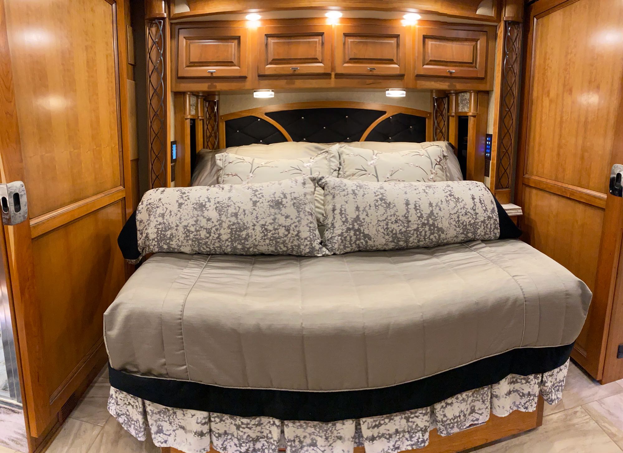 Spacious RV bedroom with a large, neatly made bed, ornate headboard, and wooden cabinetry. Ideal for an RV rental.. Tiffin Motorhomes Allegro Bus 2018