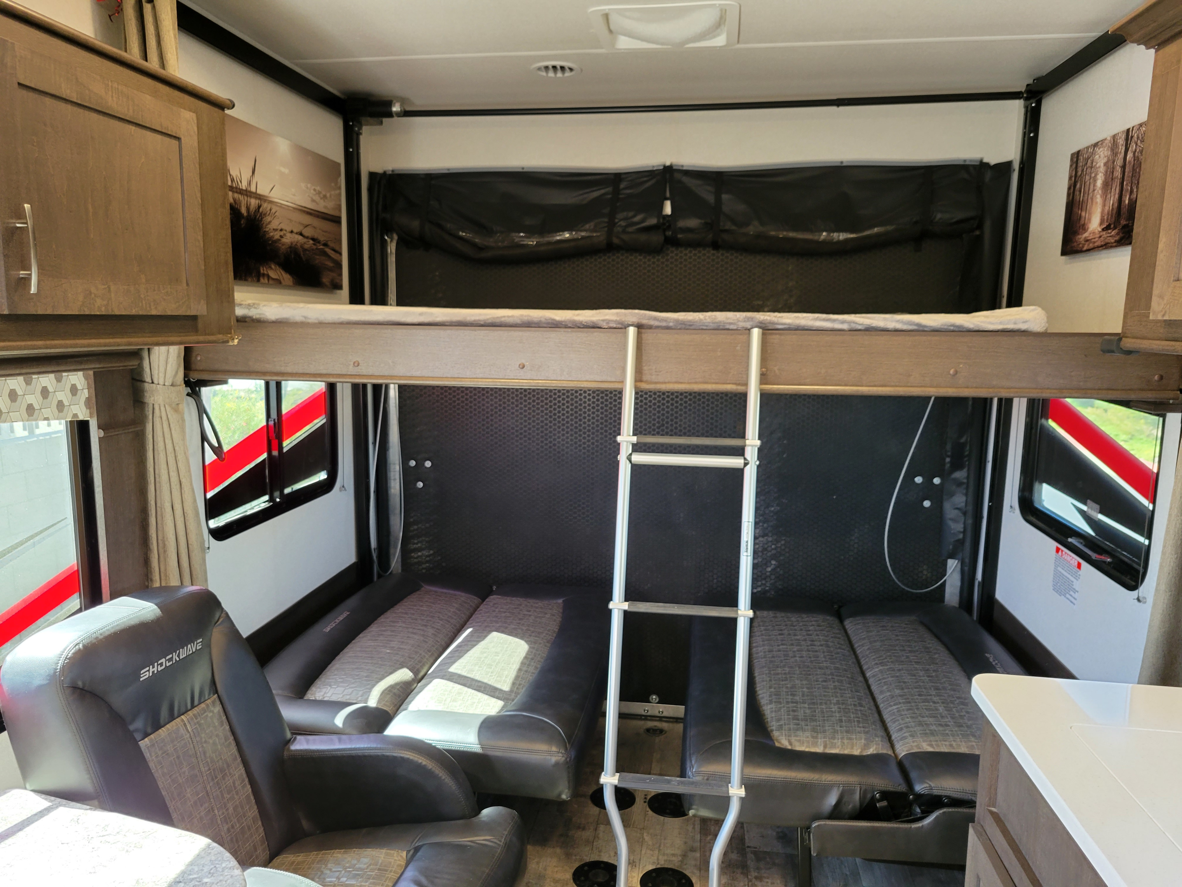 RV rental interior: versatile living space with overhead bunk beds, a ladder, and fold-down sofas below.. Forest River Shockwave 2020