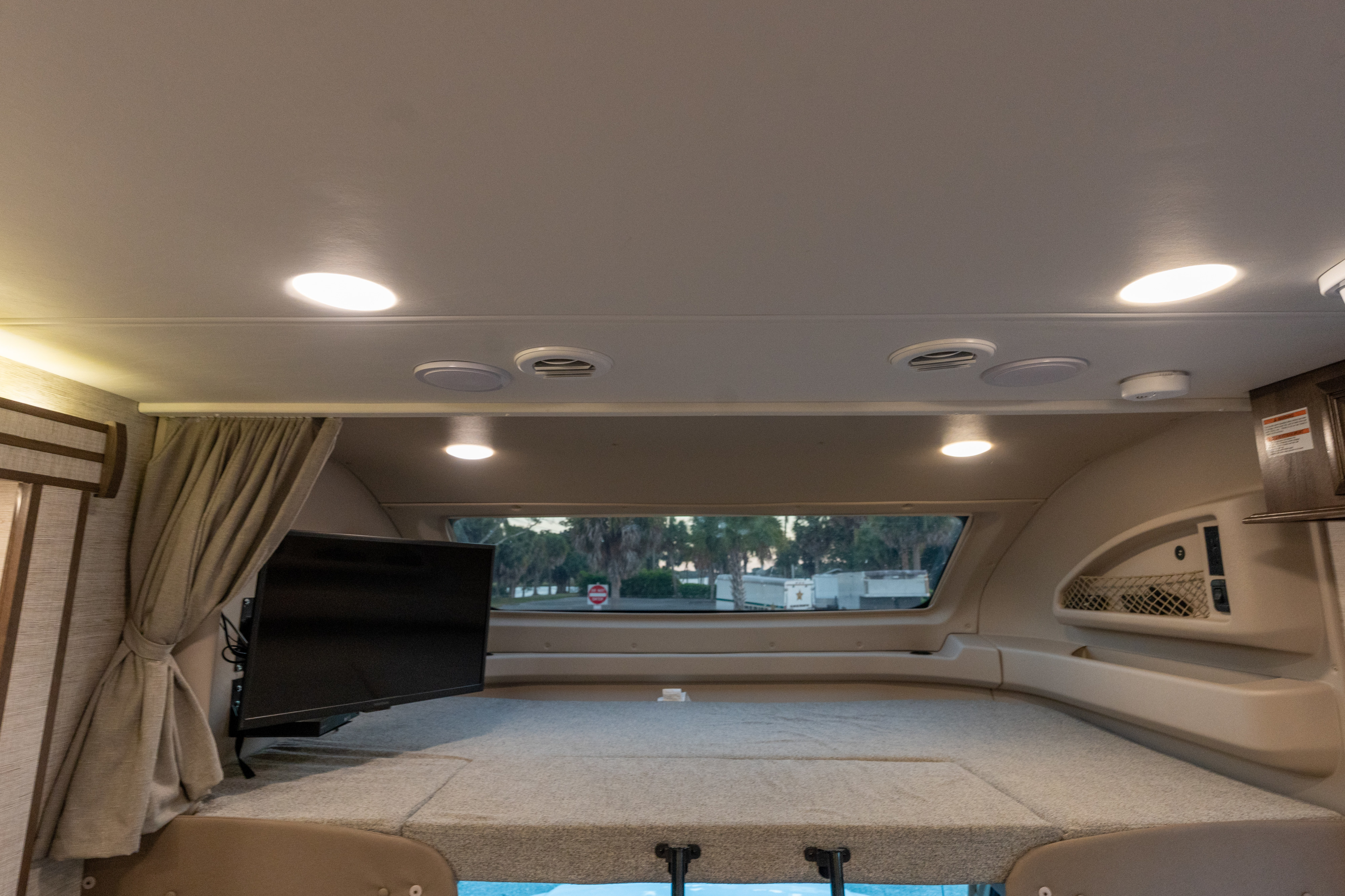 This RV rental offers a cozy, well-lit cab-over bunk with a mounted TV and window view, ideal for relaxing on the road.. Entegra Coach Esteem 31F 2021