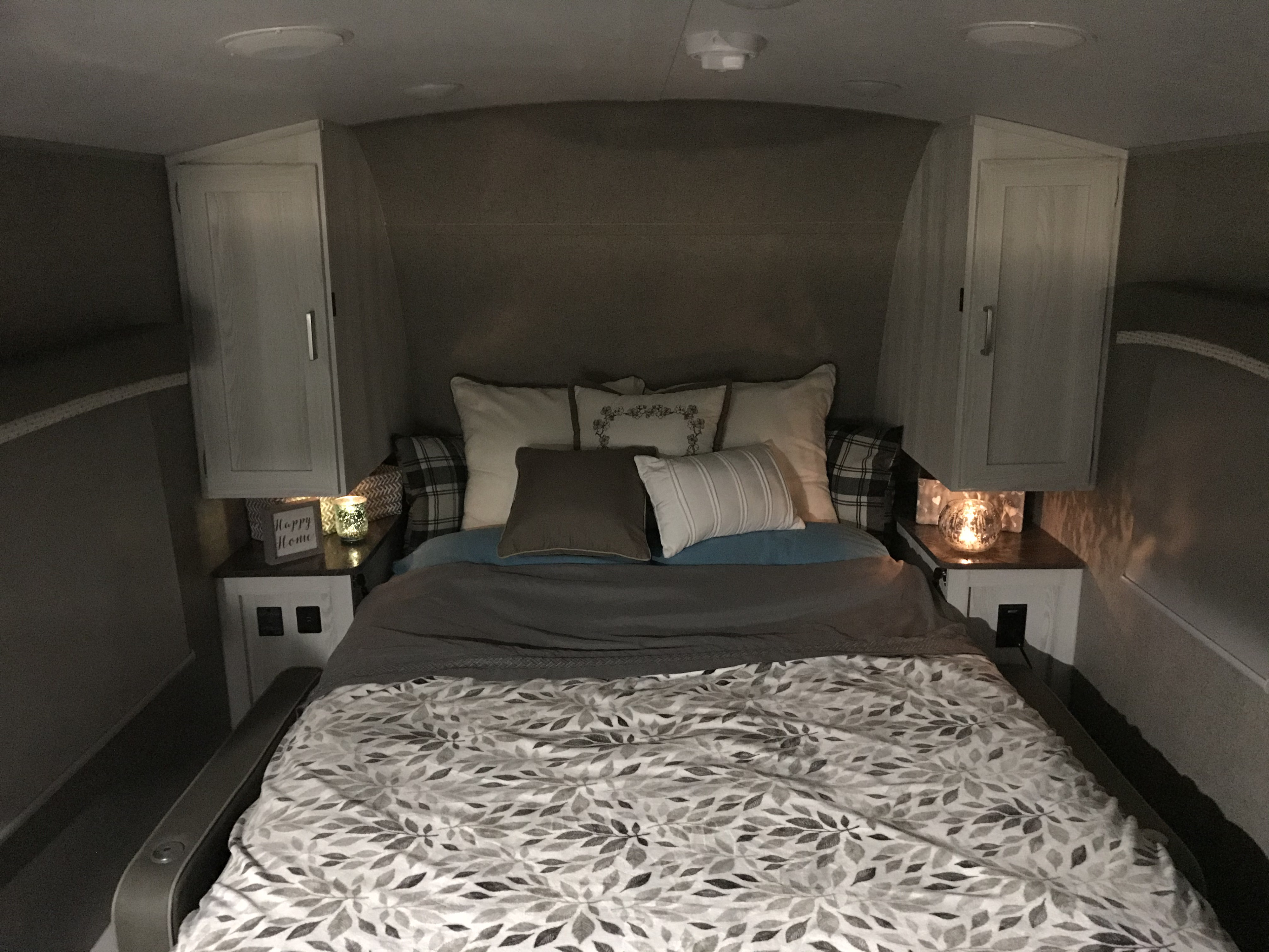 Comfortable RV rental bedroom with leaf-patterned bedding, side cabinets, and warm ambient lighting for a relaxing stay.. Forest River Rockwood 2021