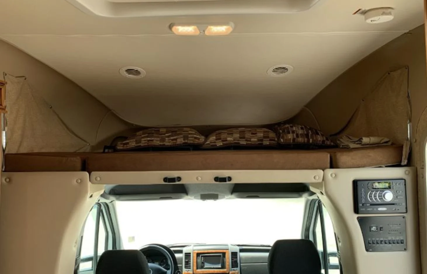 RV rental interior: cozy cab-over bunk with pillows above the driver's cockpit. Control panel and entertainment system visible.. Thor Motor Coach Citation 2015