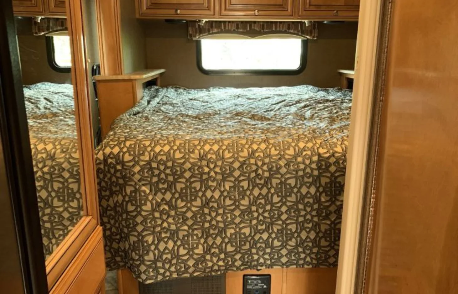 Cozy RV rental bedroom featuring a patterned bed, overhead cabinets, and a window. Perfect for your next road trip adventure.. Thor Motor Coach Citation 2015