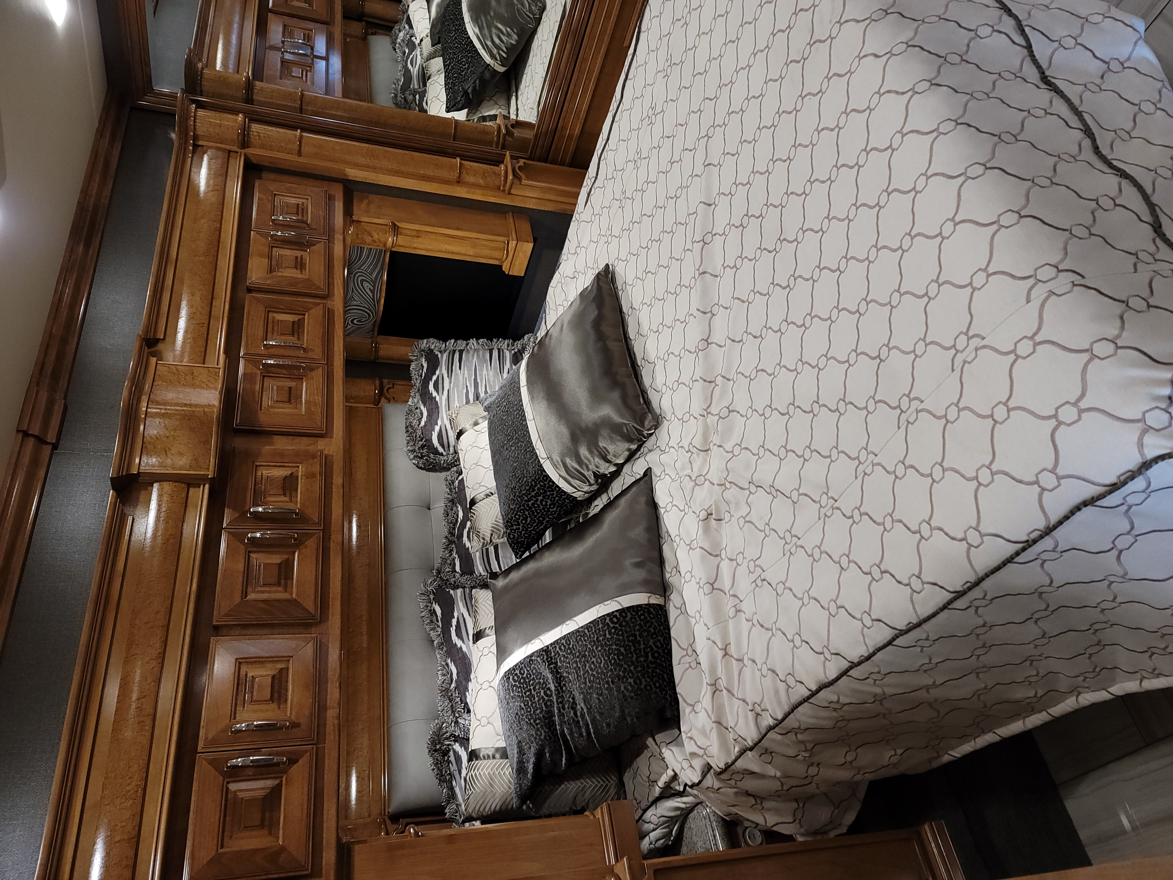 Luxurious RV rental bedroom with custom wood cabinets, patterned comforter, and plush pillows.. American Revolution 2019