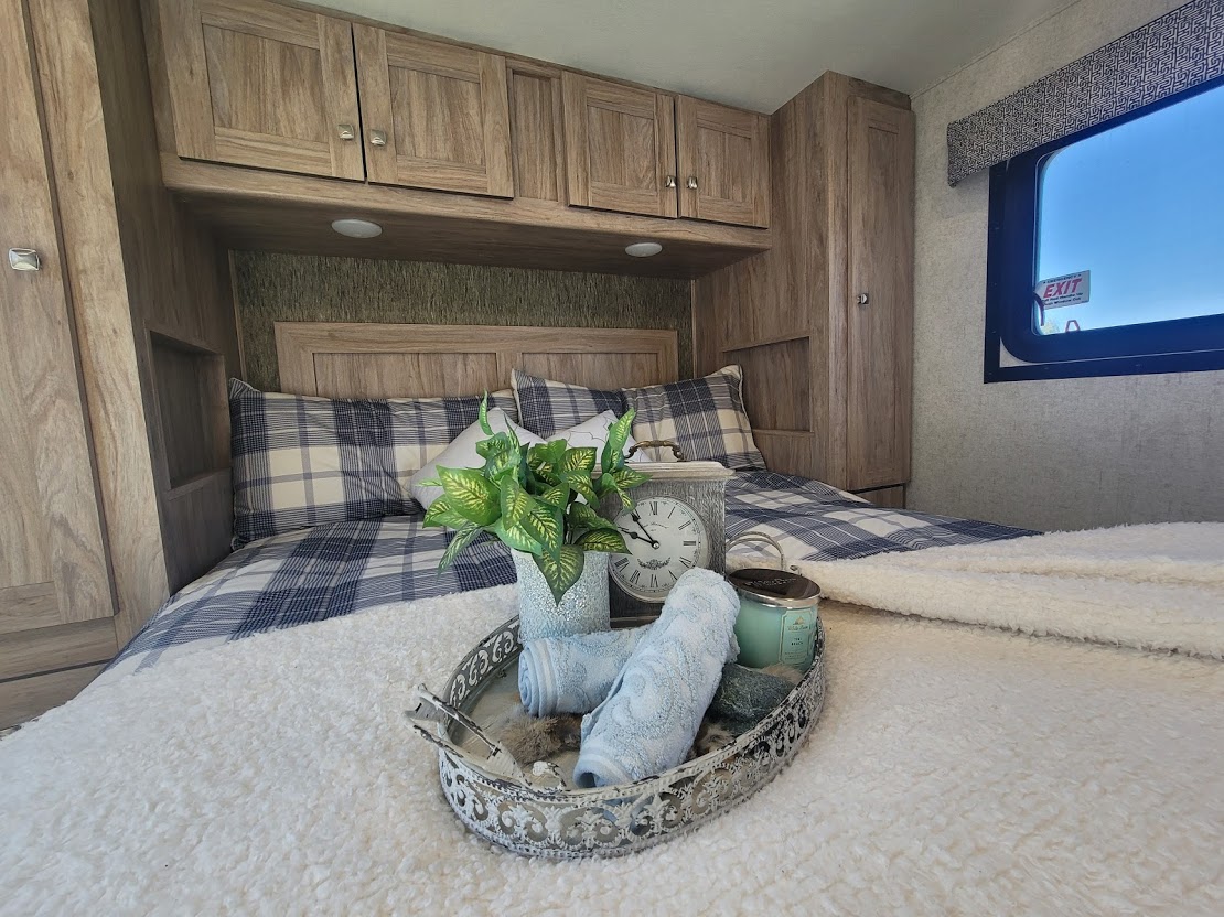 Cozy RV rental bedroom featuring plaid bedding, overhead wood cabinets, and a decorative tray with plants & towels.. Forest River Sunseeker 2019