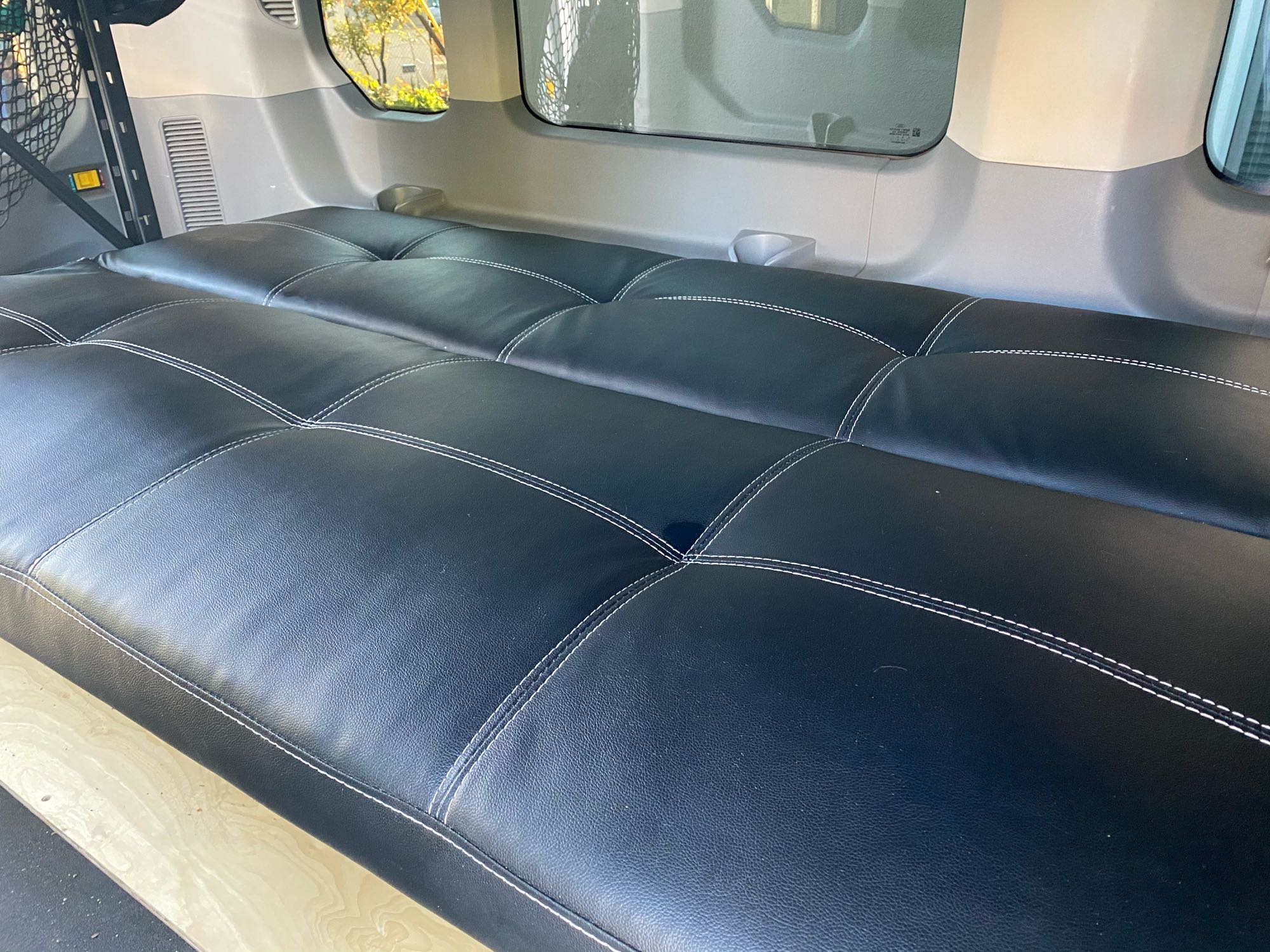 Inside an RV rental: a plush black bed with white stitching and custom wooden platform for comfort.. Ford 350 2015