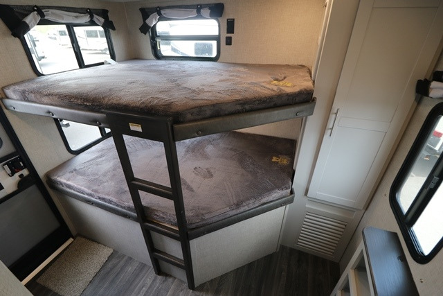 Interior view of an RV rental featuring bunk beds with windows and a ladder, offering comfortable sleeping accommodations.. Keystone RV Bullet Ultra Lite 2021