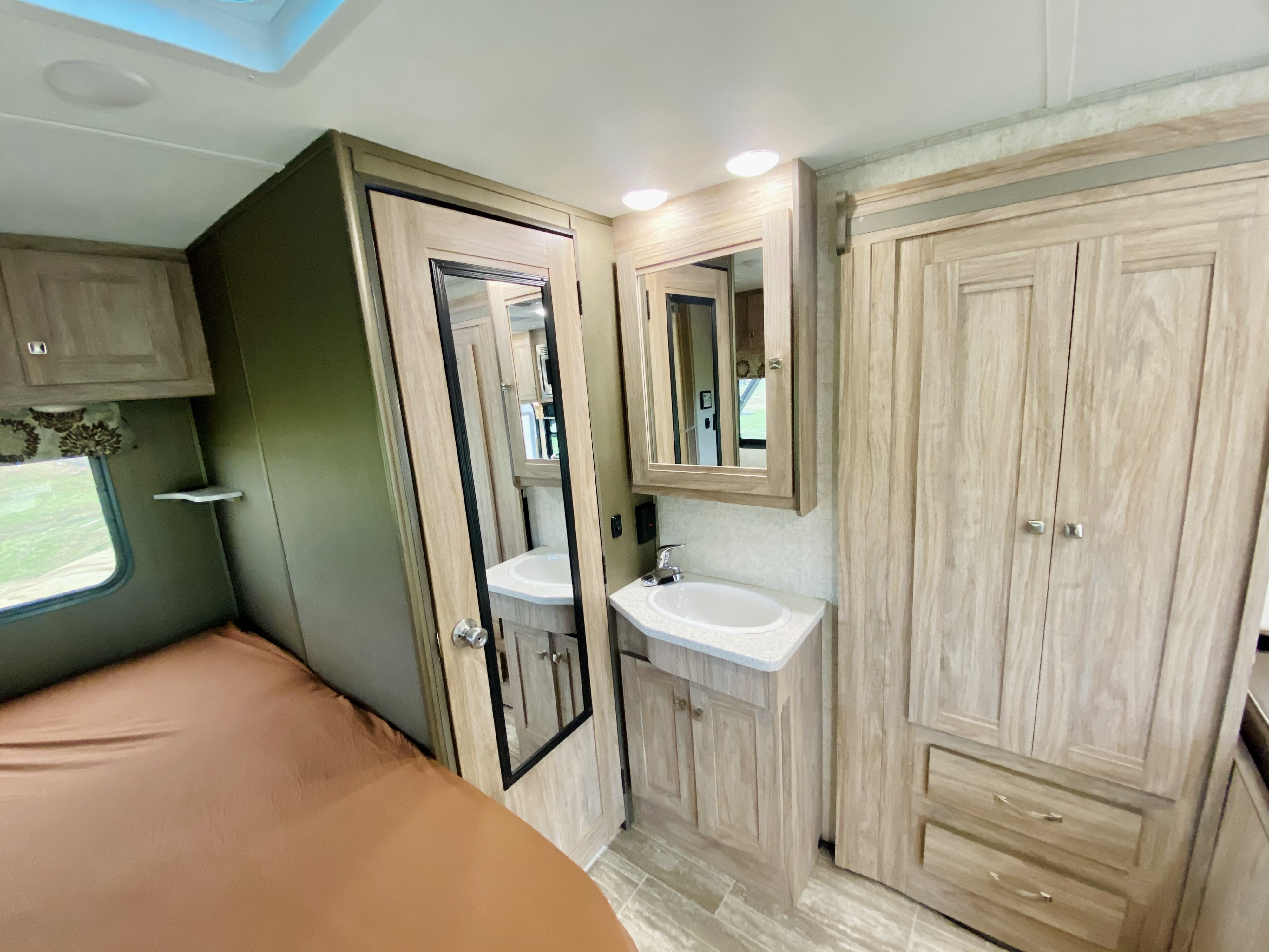 RV rental interior: cozy bedroom area with window, adjacent vanity with sink/mirror, and large wardrobe storage.. Forest River Forester 2020