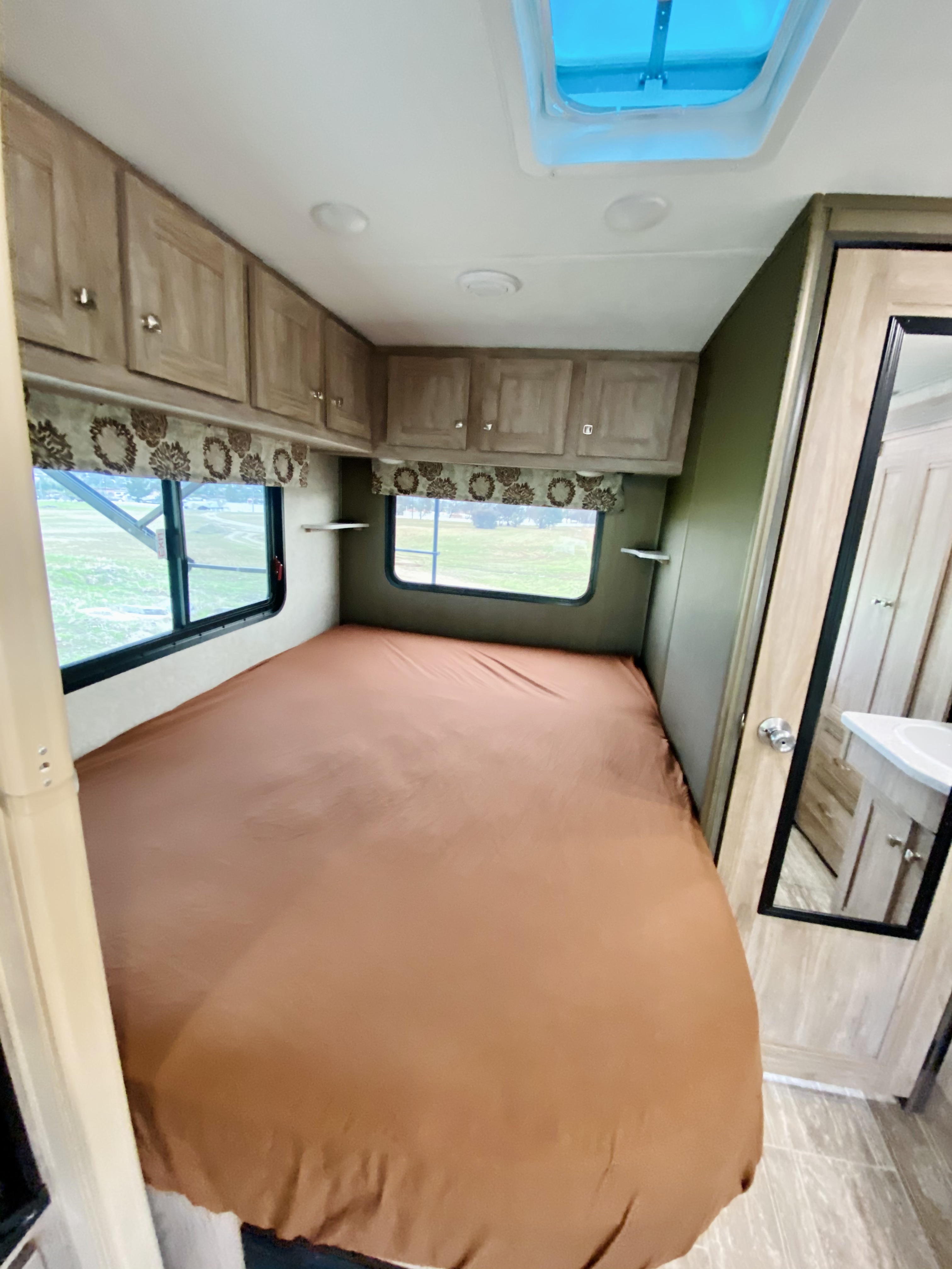 Inside an RV rental bedroom: a brown bed, windows, and light wood cabinets line the walls. A skylight brightens the ceiling.. Forest River Forester 2020