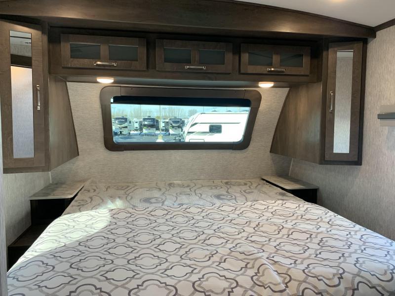 This comfortable RV rental bedroom features a large bed, overhead storage, and a window view, perfect for travel.. Dutchmen Denali 2021