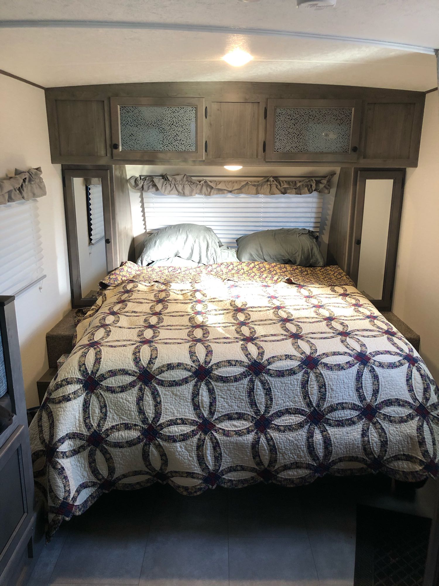 Cozy RV rental bedroom featuring a patterned quilt, overhead cabinets, and side storage. Ideal for travelers.. Other Other 2021