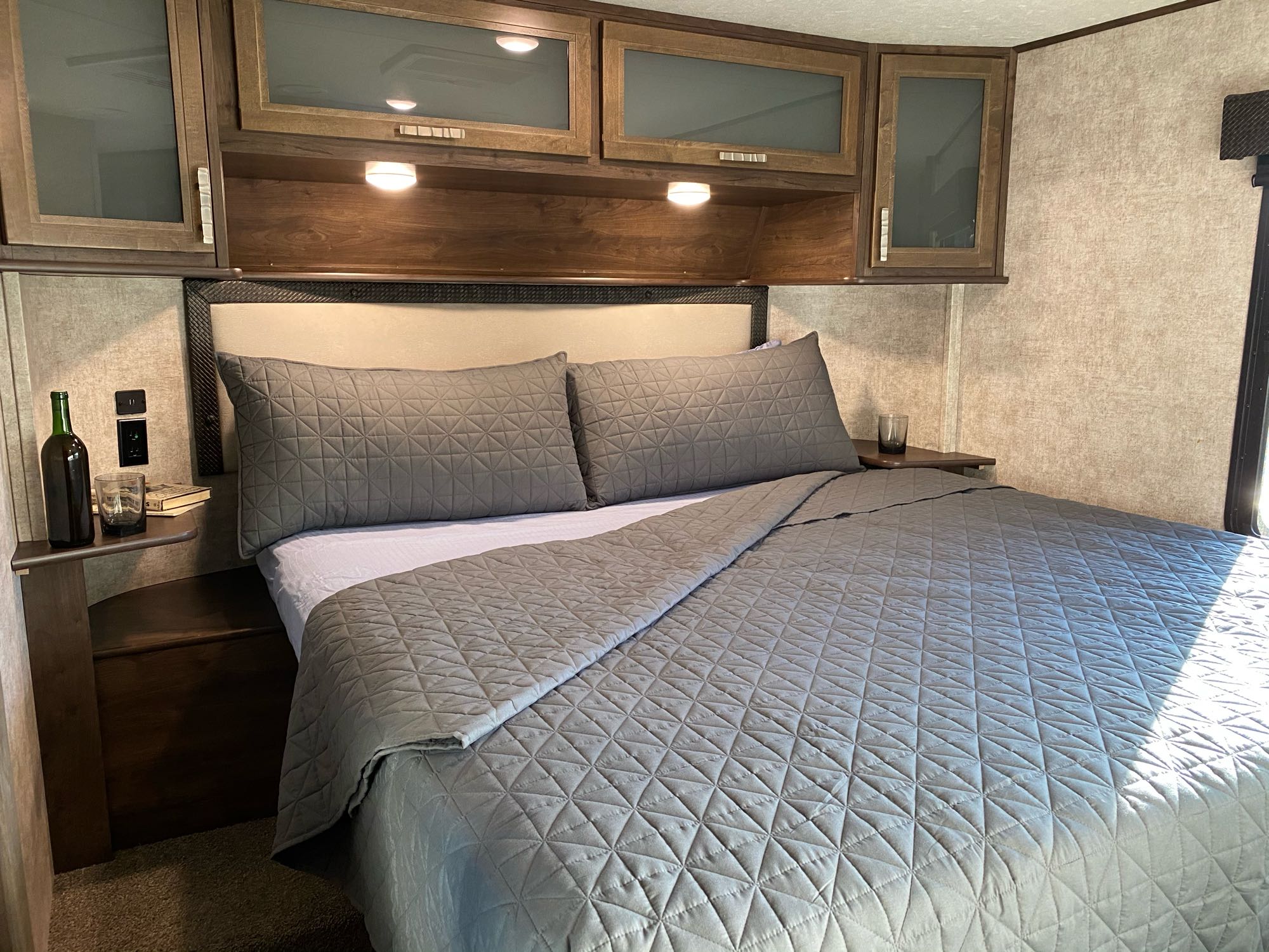 Cozy RV rental bedroom featuring a large bed with grey quilted bedding and overhead cabinets for a comfortable stay.. Open Range Highlander 2018