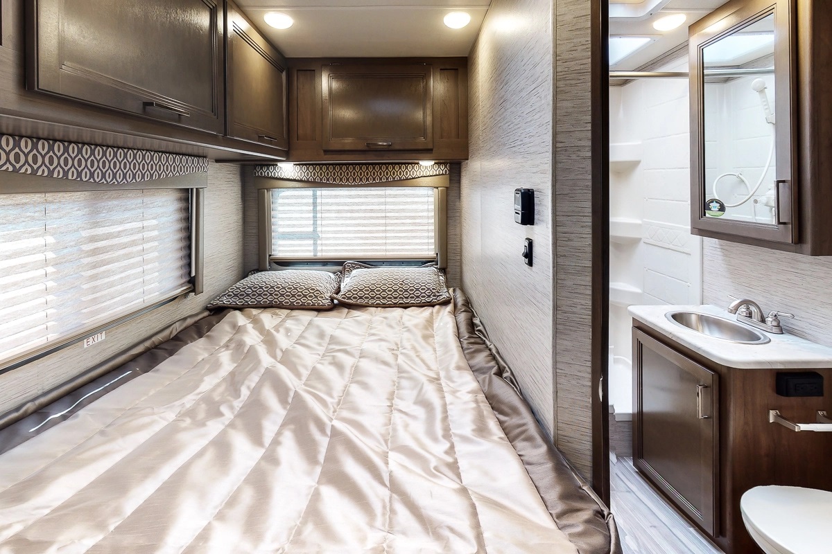 Comfortable RV rental interior: bedroom with bed, overhead cabinets, and compact bathroom with sink & shower.. Thor Motor Coach Freedom Elite 2021