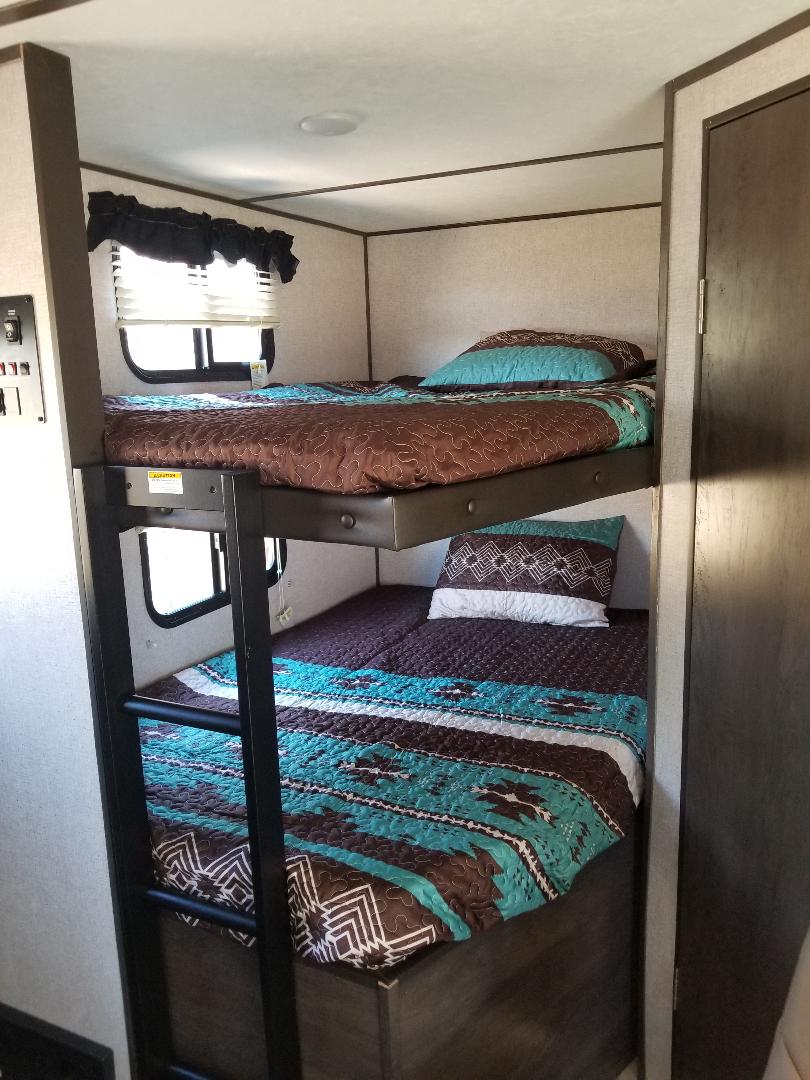 Inside an RV rental: two bunk beds with colorful Southwestern-style bedding, a ladder, and a window for comfortable sleeping.. Dutchmen Coleman 2021