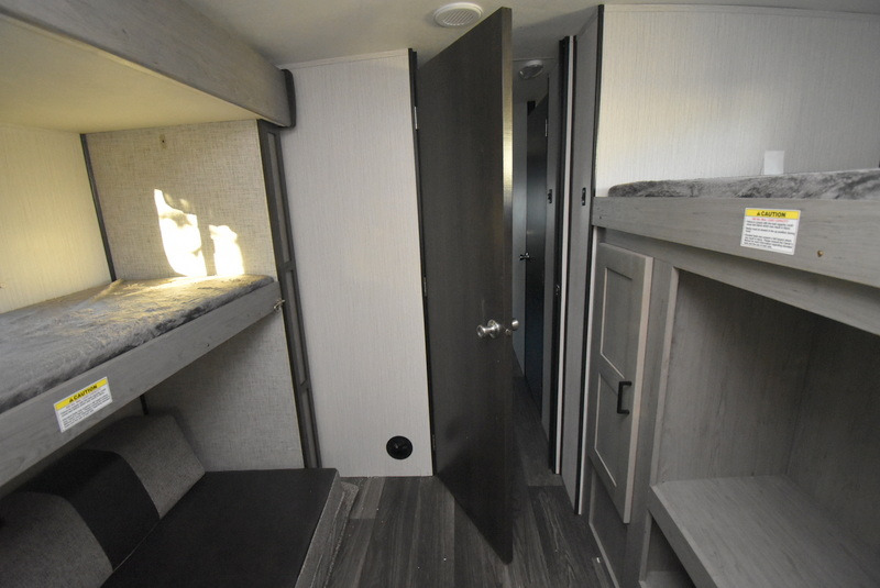 Bright RV rental interior showcases bunk beds, one with lower seating & sunlit wall, the other with storage. Door to another room.. Other M-3385 2020