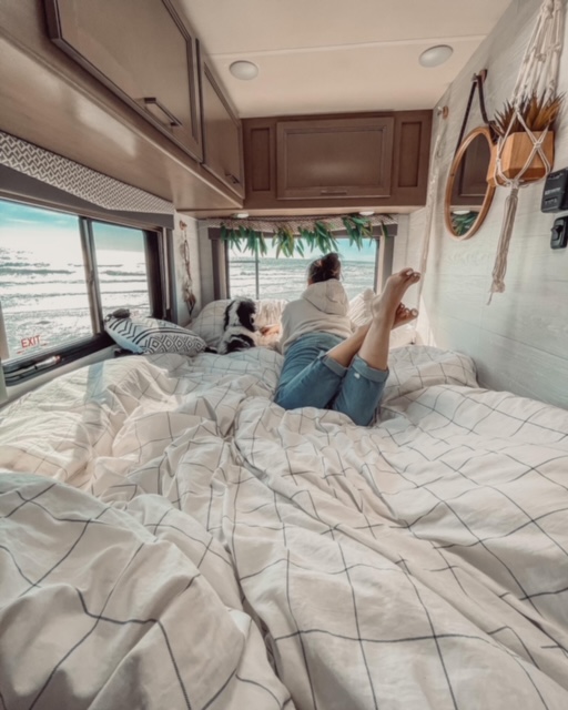 Cozy RV rental bedroom with ocean views, a person and their dog enjoying the perfect travel setup.. Thor Four Winds 2021