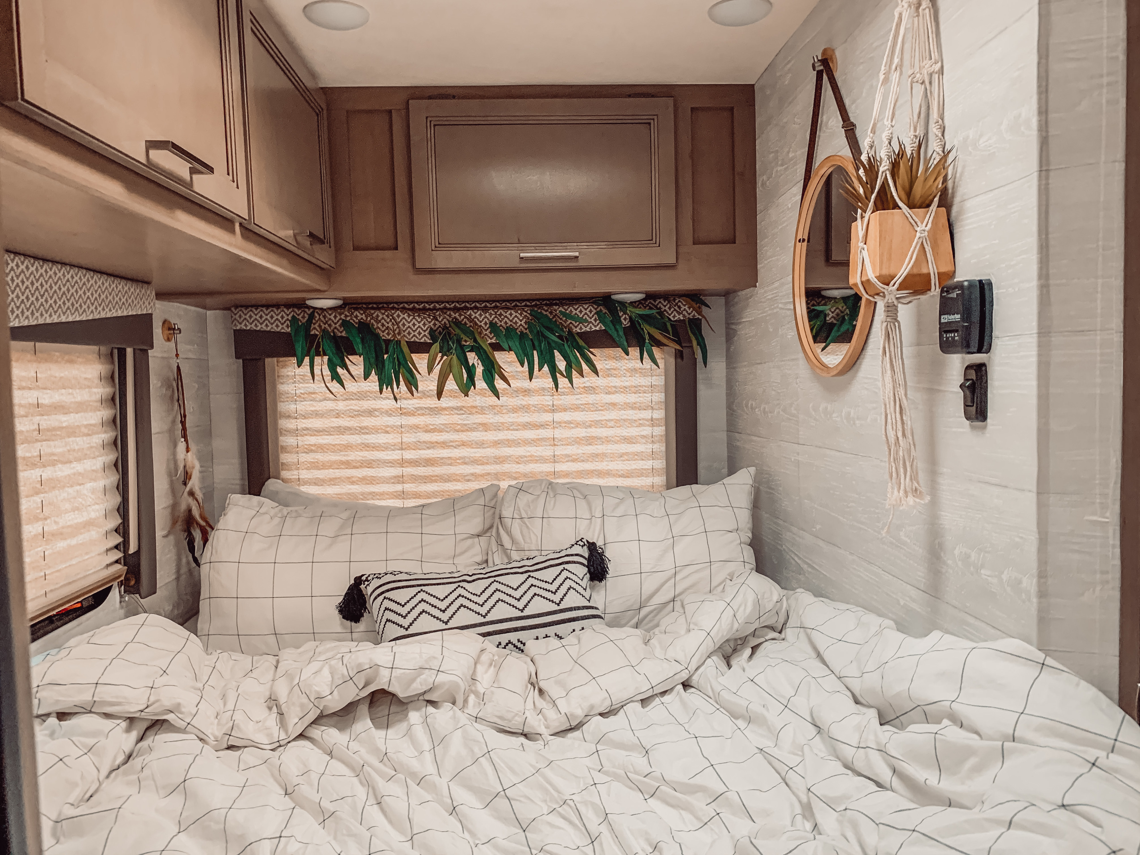 Cozy RV rental bedroom: white grid bedding, wooden cabinets, window blinds, and stylish decor including a hanging plant and mirror.. Thor Four Winds 2021