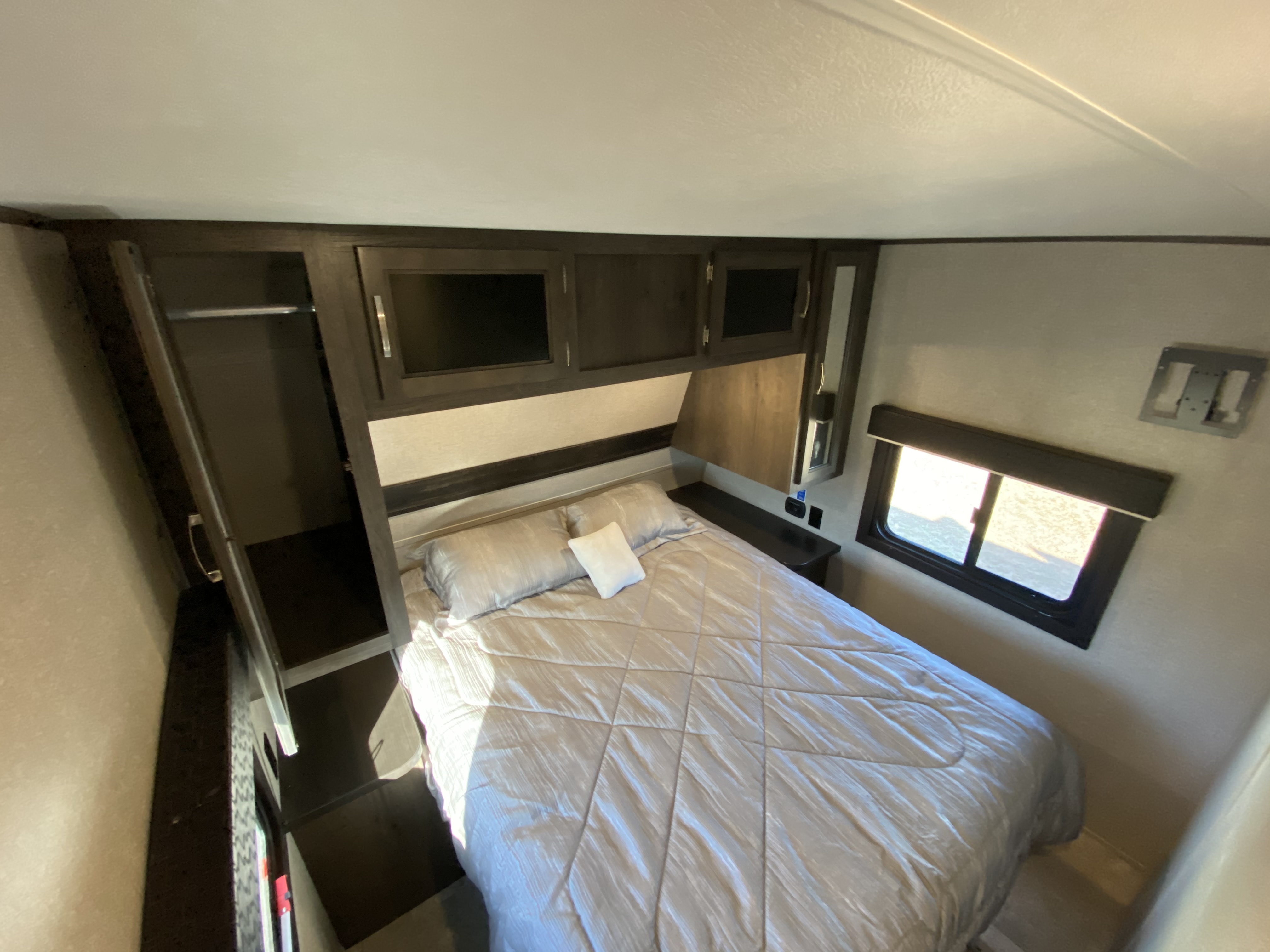 Interior of an RV rental bedroom with a neatly made bed, dark wood cabinets, a wardrobe, and a bright window.. Jayco Jay Flight 2021